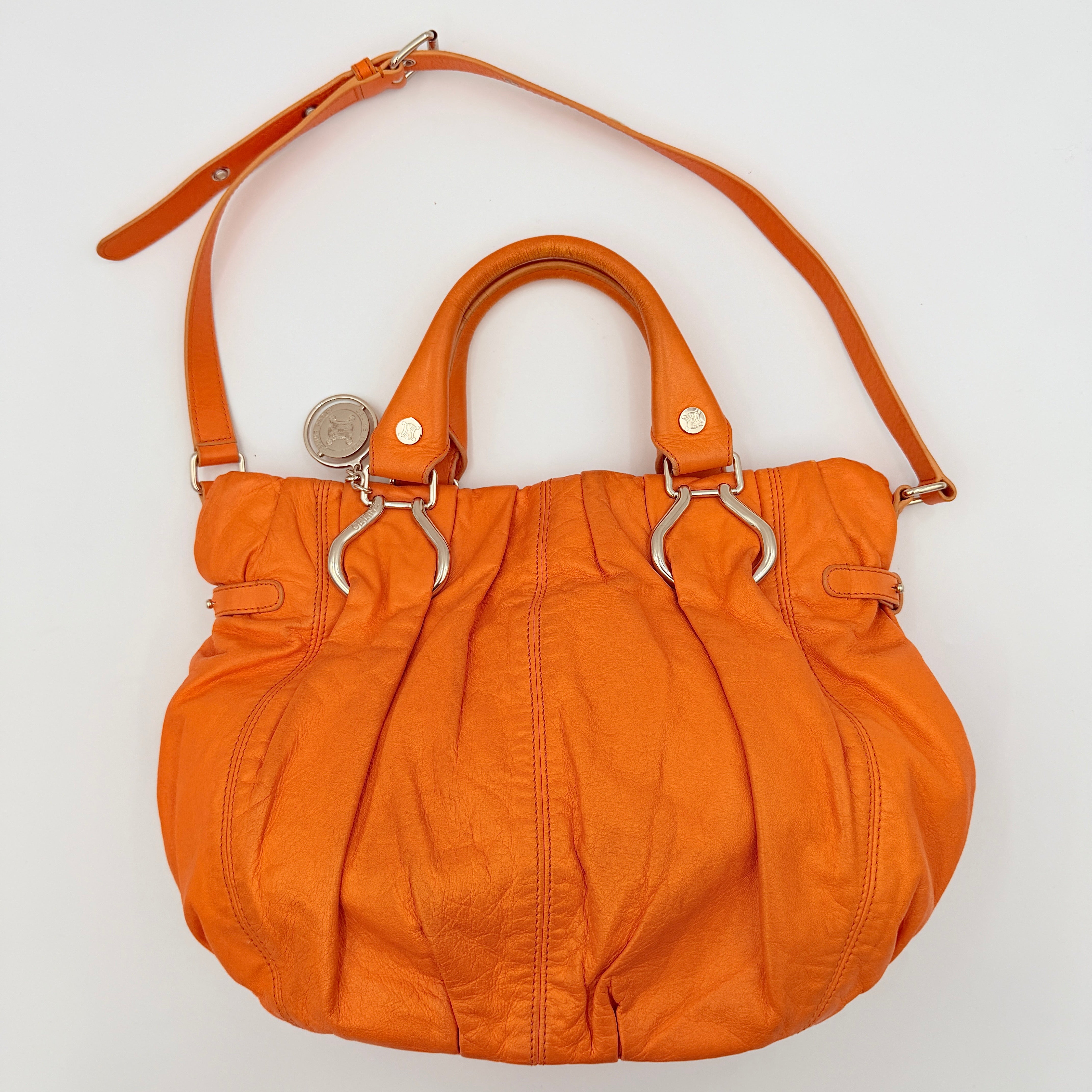 Celine 2Way Shoulder Bag in vibrant orange leather with silver-tone hardware and pleated detailing, shown with both top handles and an adjustable strap.