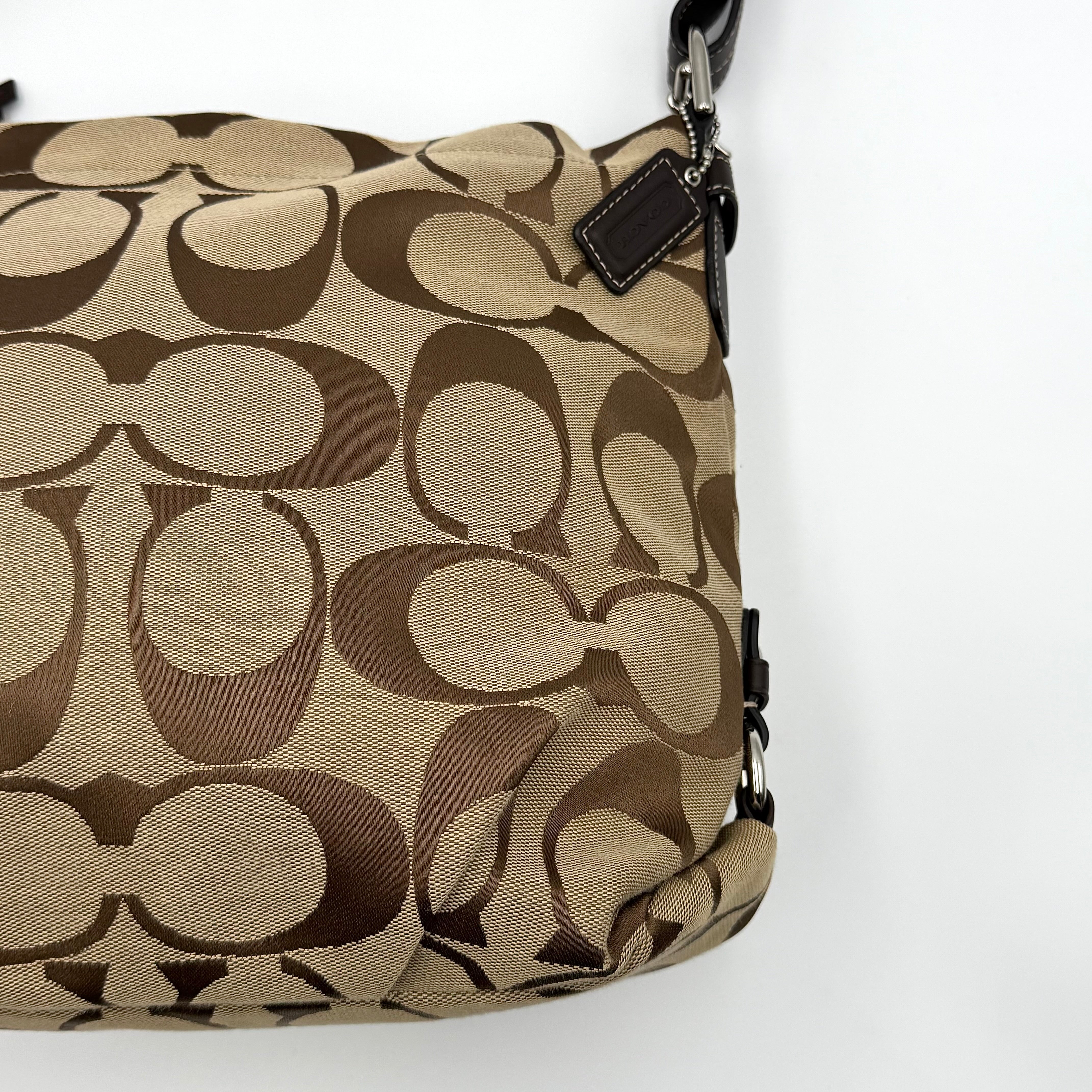 Coach beige and brown signature canvas hobo shoulder bag with black leather strap and silver hardware shown on a white background.