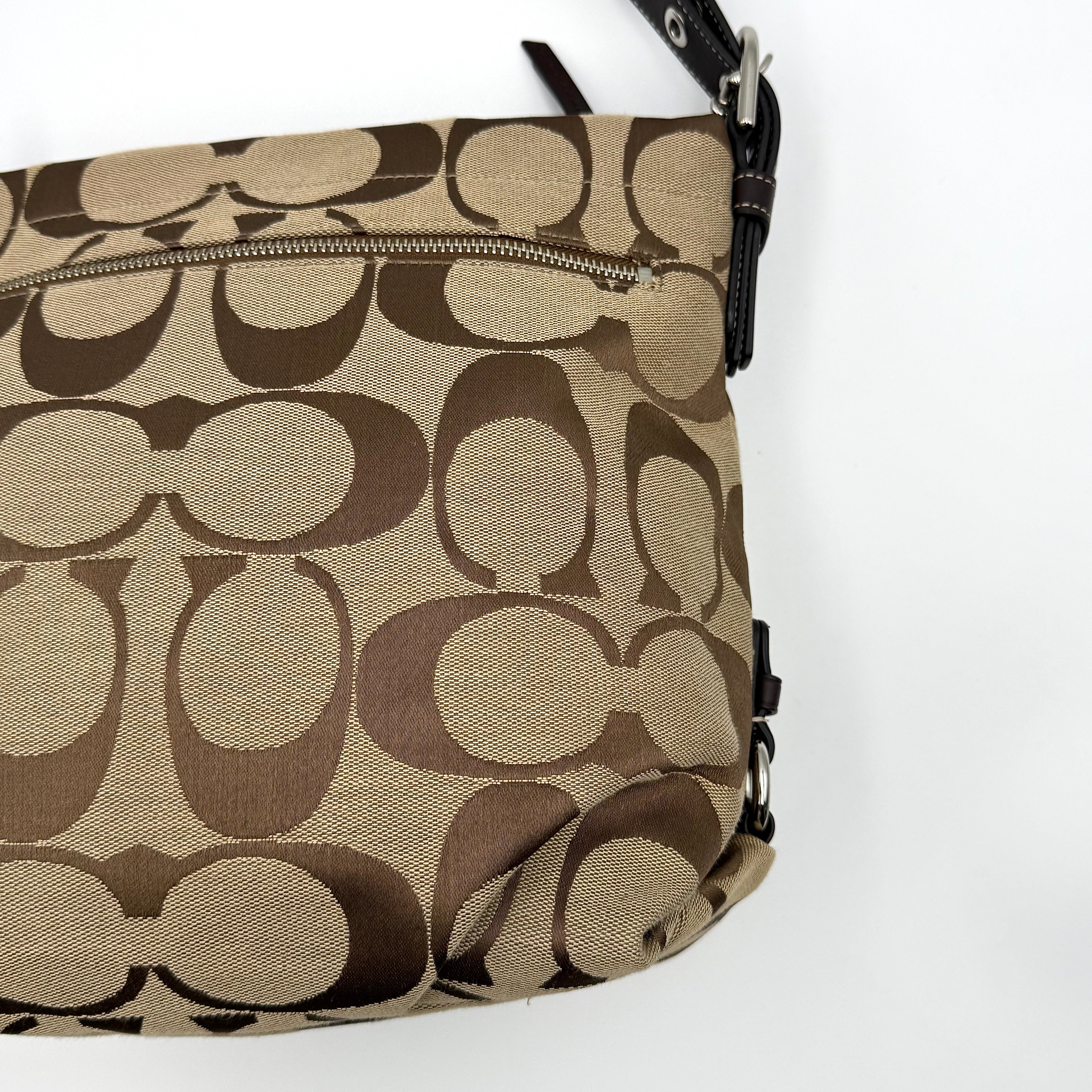 Coach beige and brown signature canvas hobo shoulder bag with black leather strap and silver hardware shown on a white background.