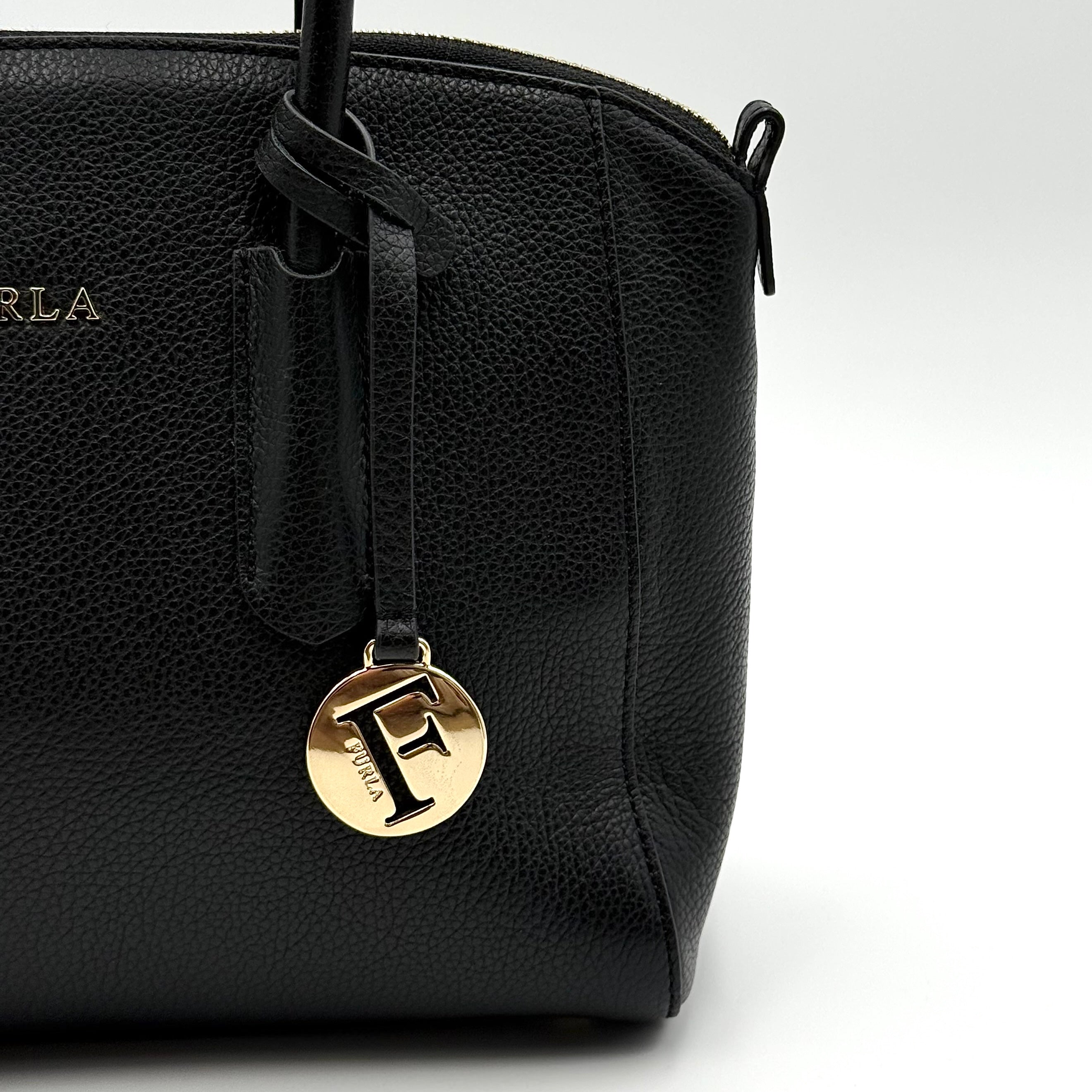 Front view of the Furla Tessa black leather satchel with gold-tone Furla charm and structured silhouette.