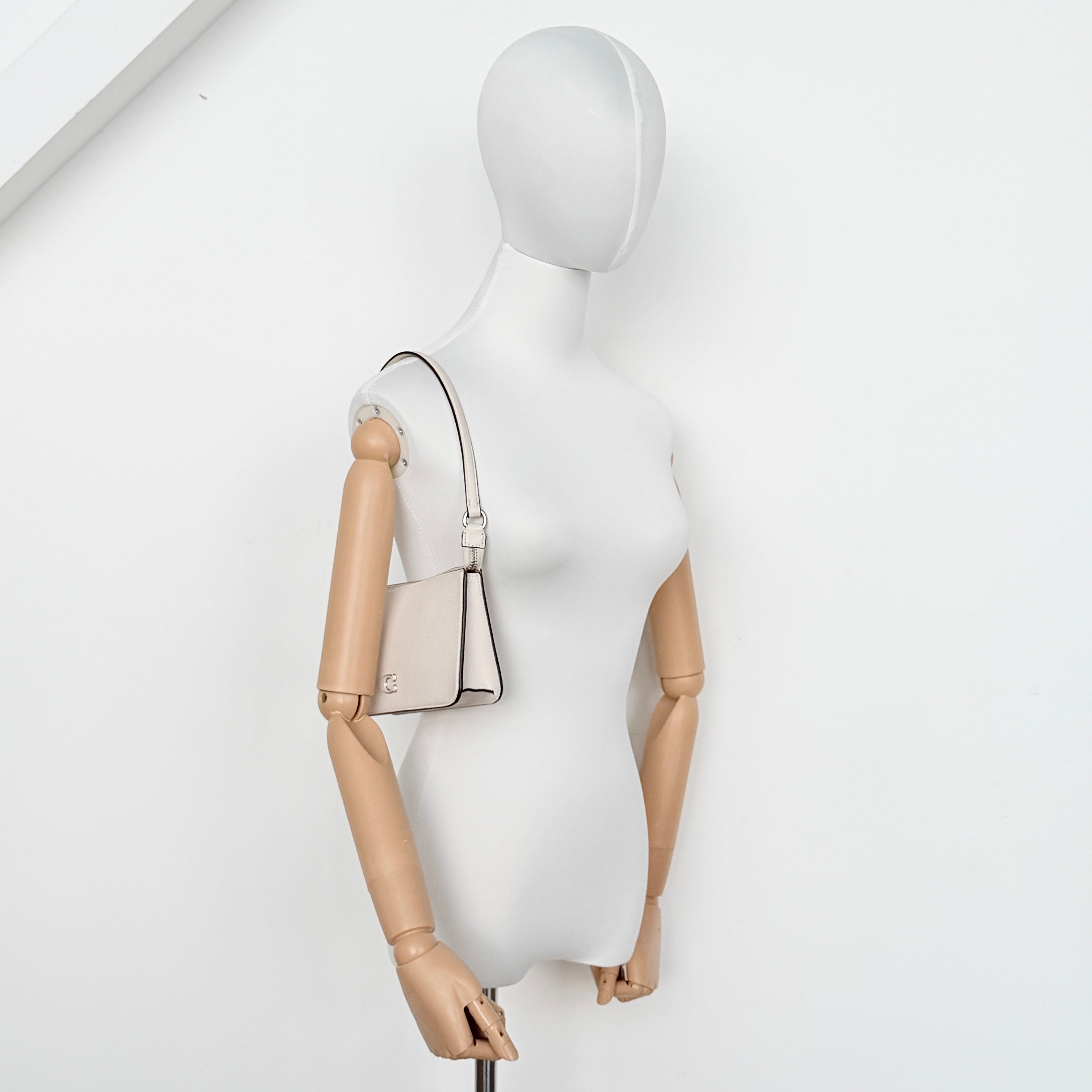 Coach cream grained leather shoulder bag with silver logo plaque and structured handle, displayed against a white background.