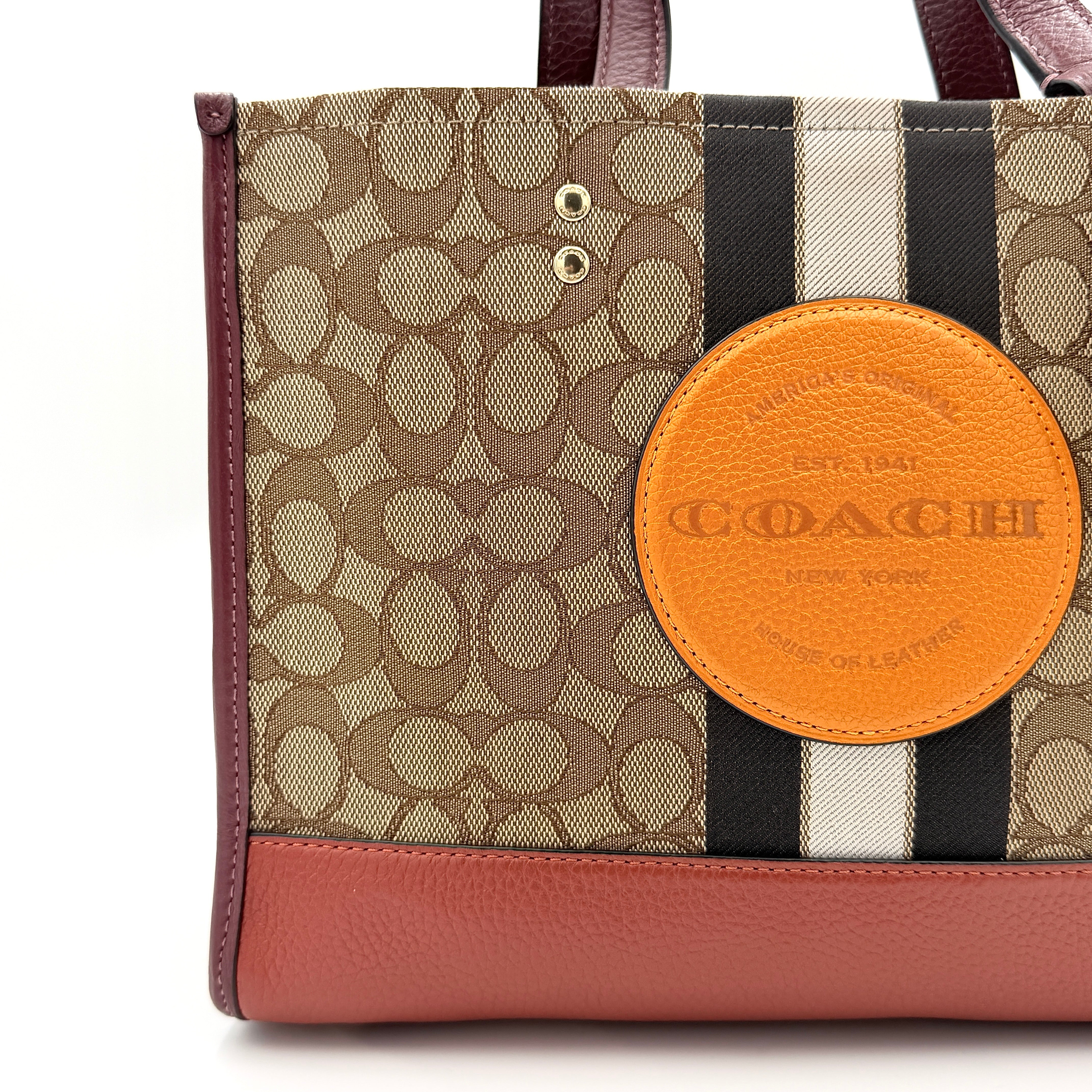 Coach 2Way Signature 22 Dempsey Tote in brown jacquard and burgundy leather with orange logo patch, shown with detachable strap.