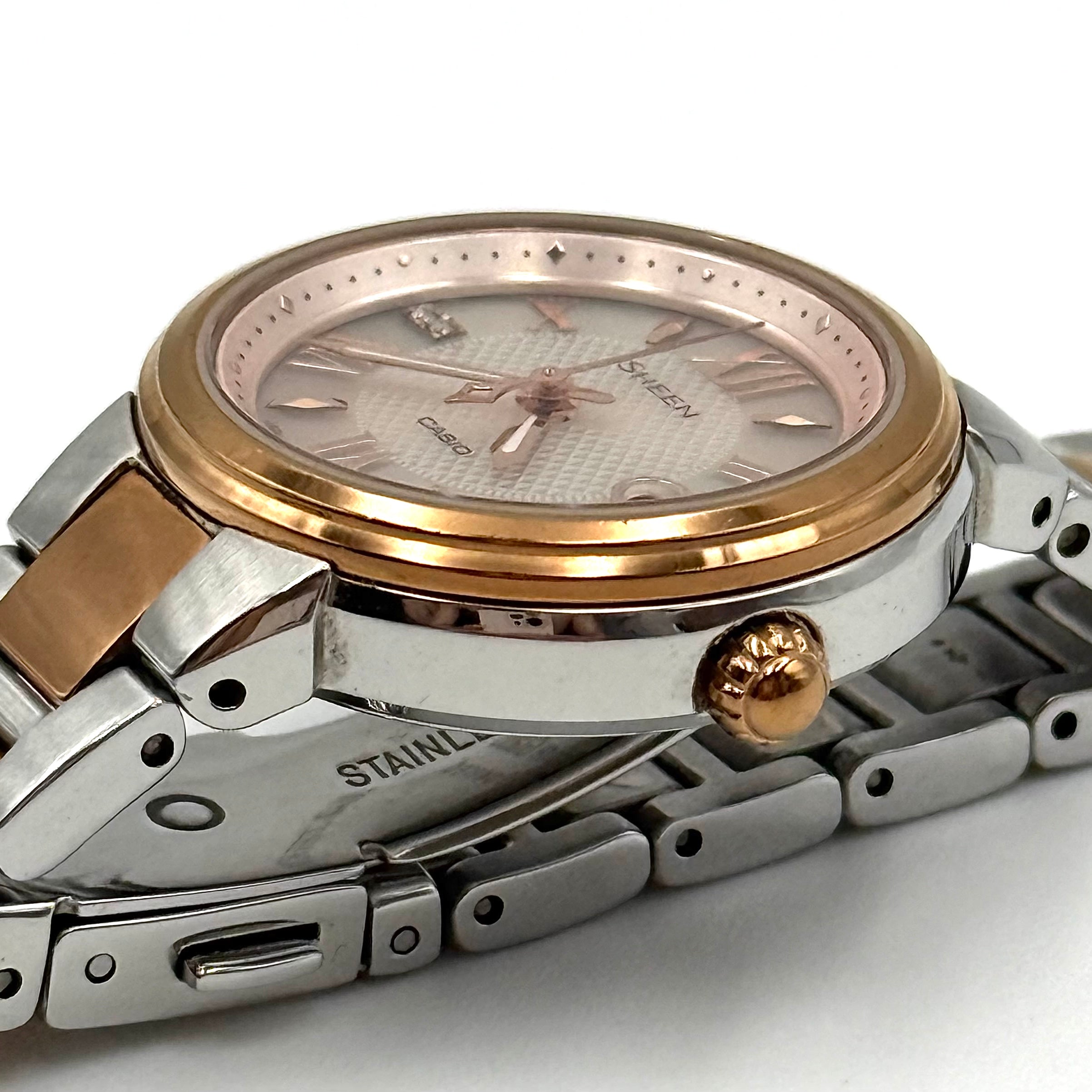 Casio Sheen SHE-4516 stainless steel watch with a rose gold and silver bracelet displayed on a black cushion.