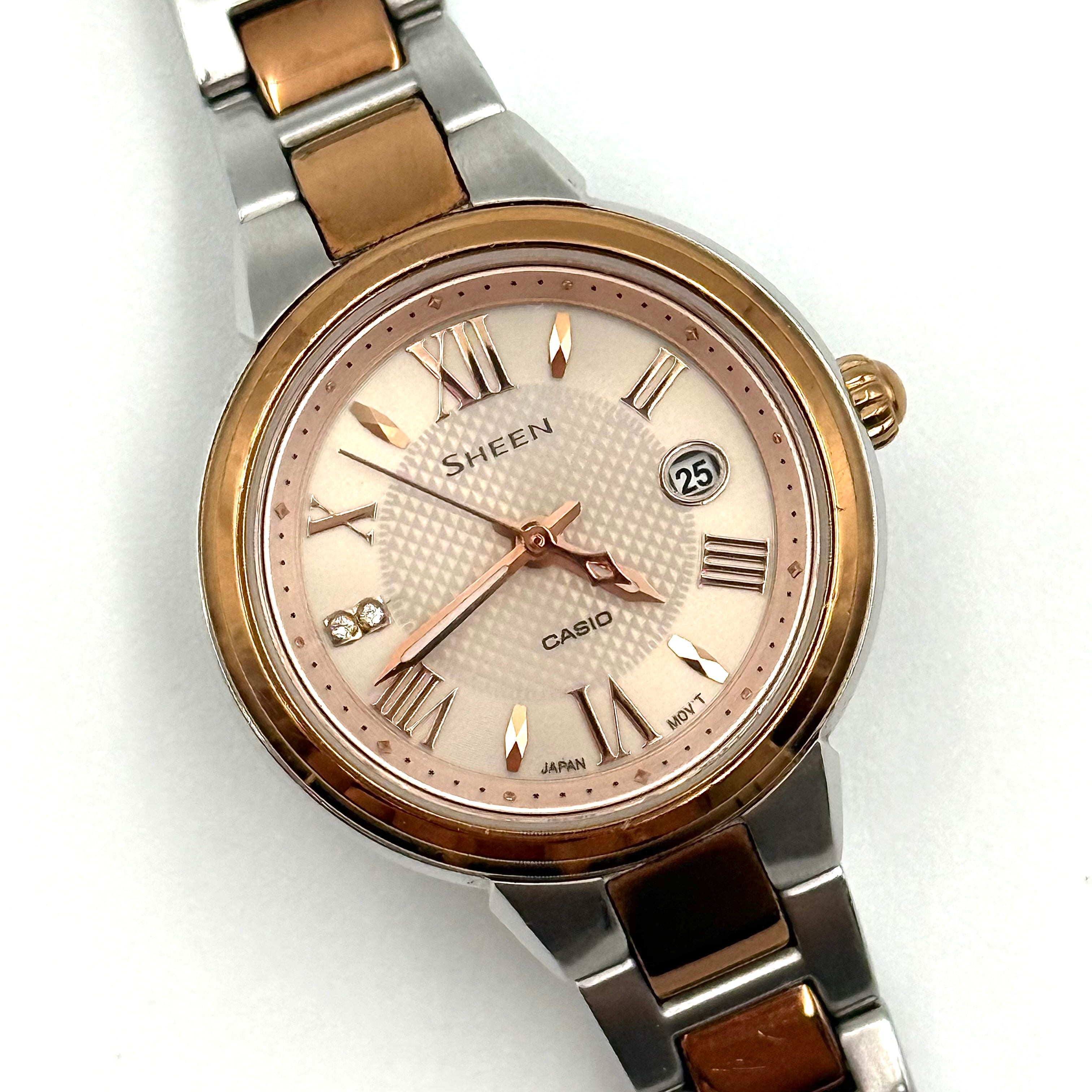 Casio Sheen SHE-4516 stainless steel watch with a rose gold and silver bracelet displayed on a black cushion.