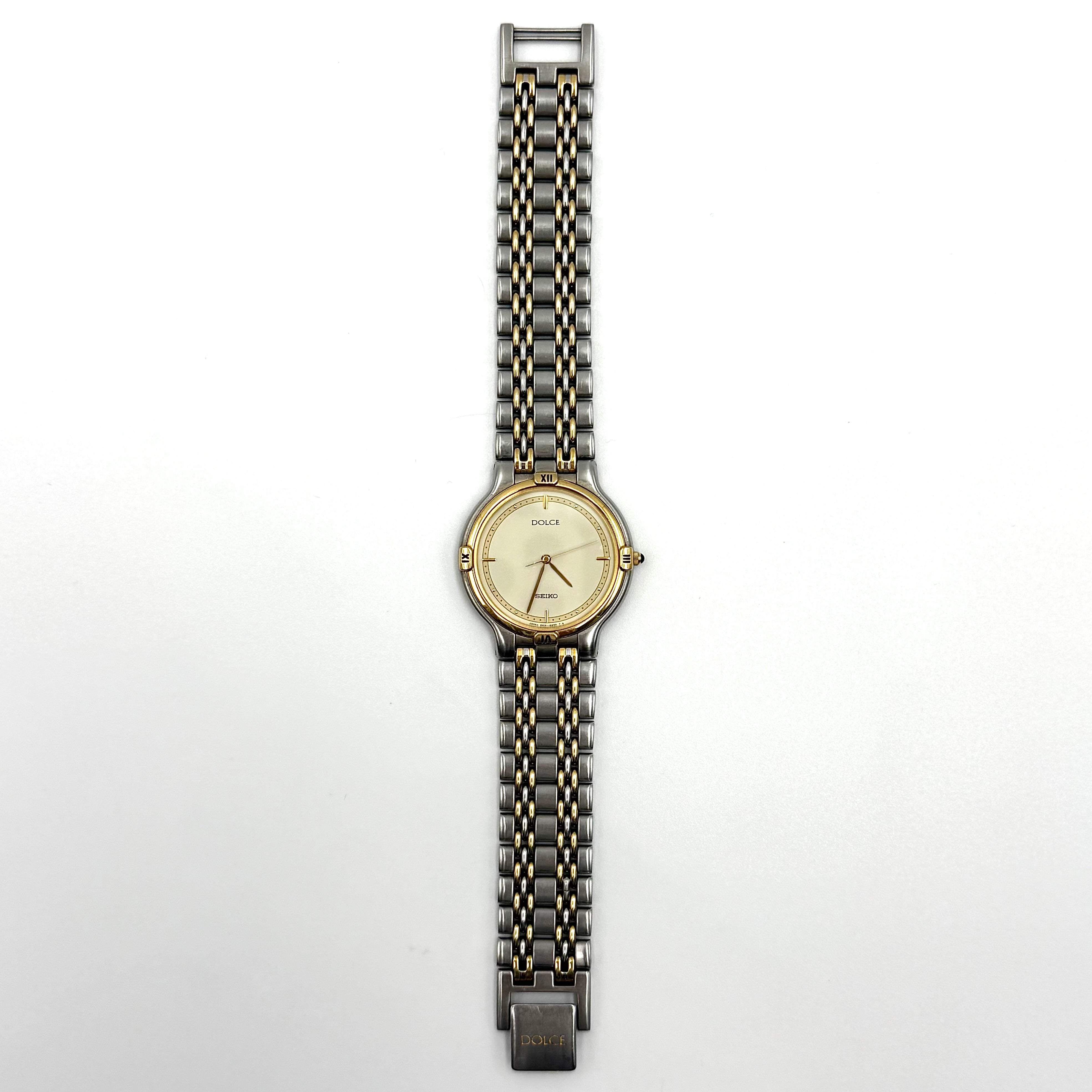 Seiko Dolce 5E31-6B90 watch in stainless steel with gold-tone accents and a cream dial, displayed on a black cushion.