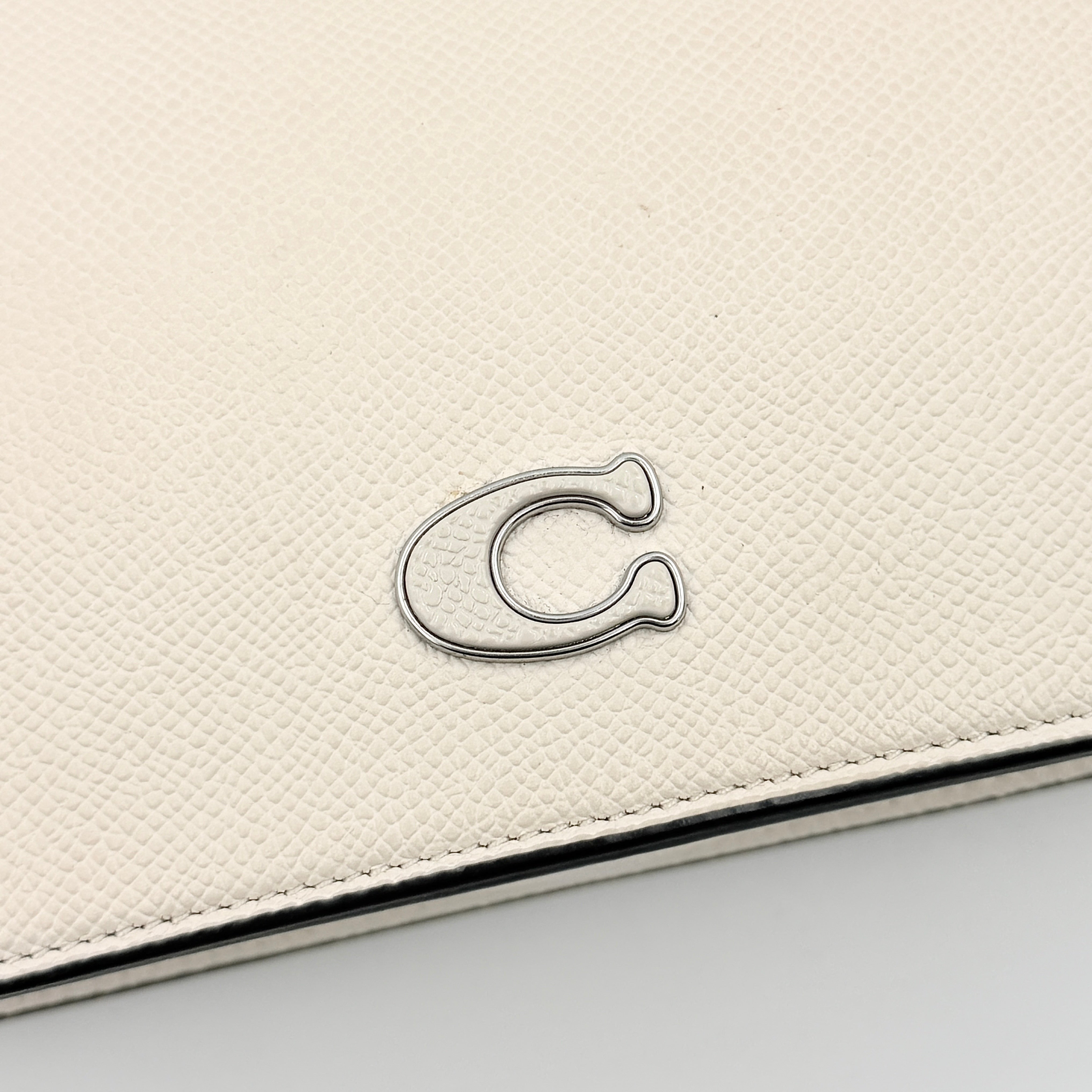 Coach cream grained leather shoulder bag with silver logo plaque and structured handle, displayed against a white background.