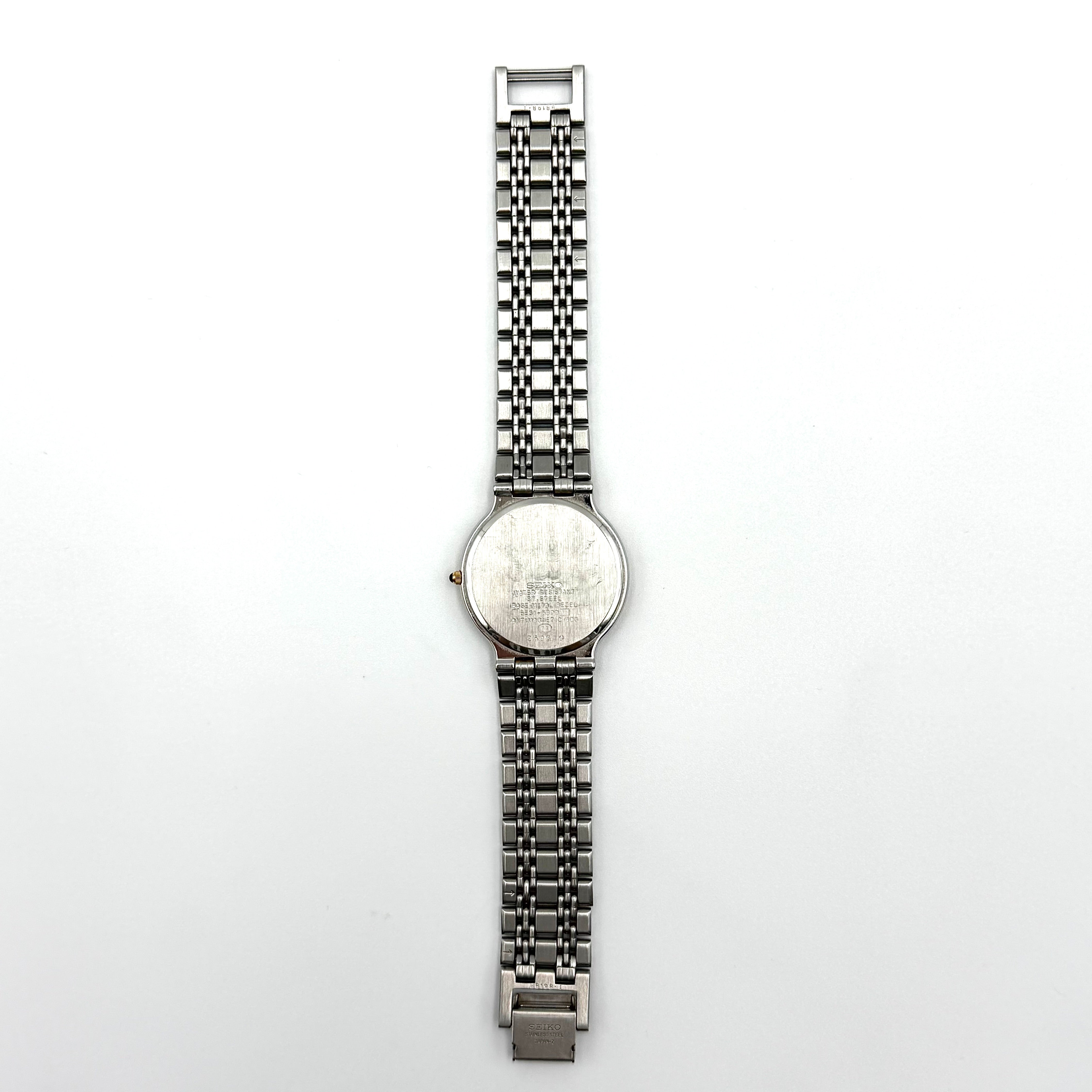 Seiko Dolce 5E31-6B90 watch in stainless steel with gold-tone accents and a cream dial, displayed on a black cushion.