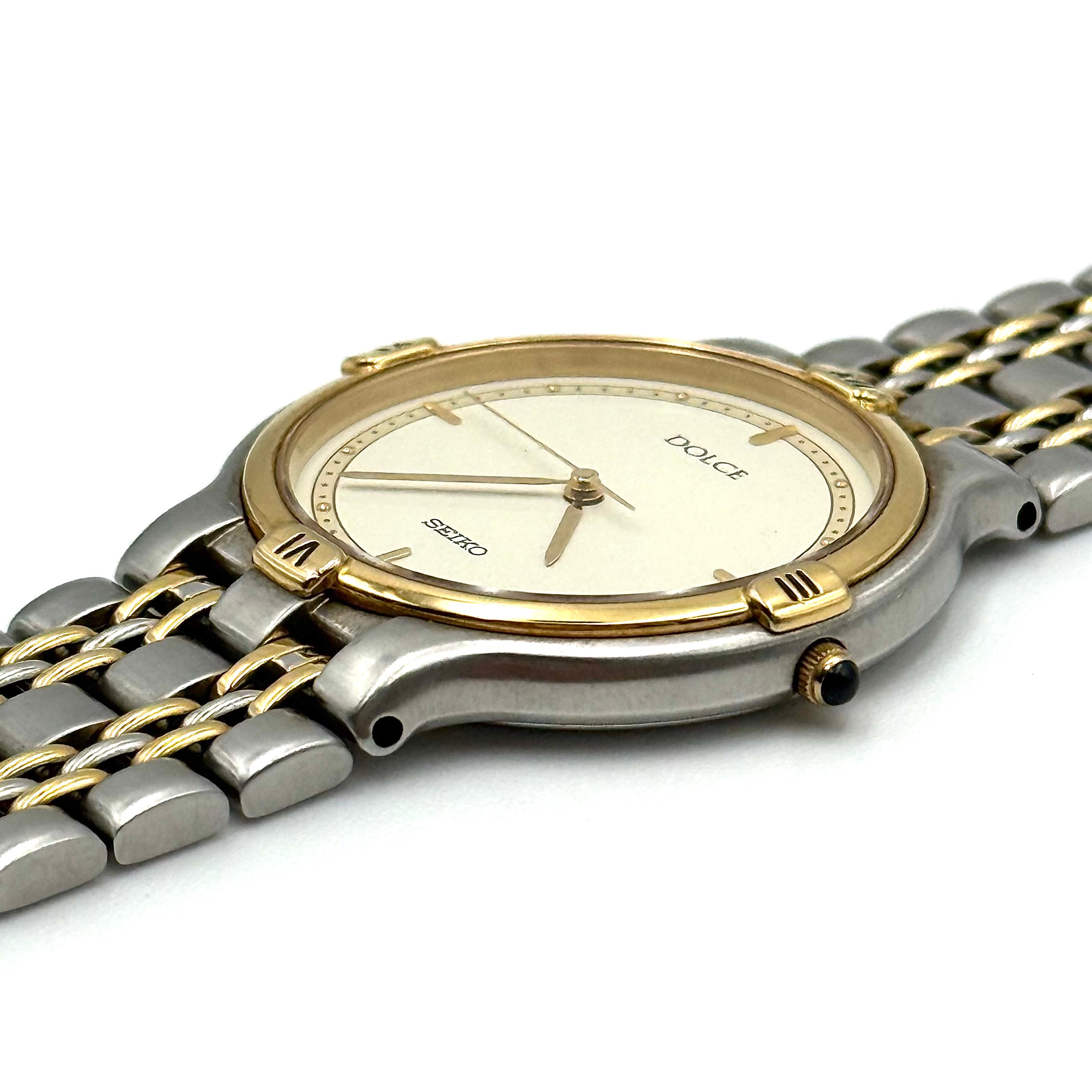 Seiko Dolce 5E31-6B90 watch in stainless steel with gold-tone accents and a cream dial, displayed on a black cushion.