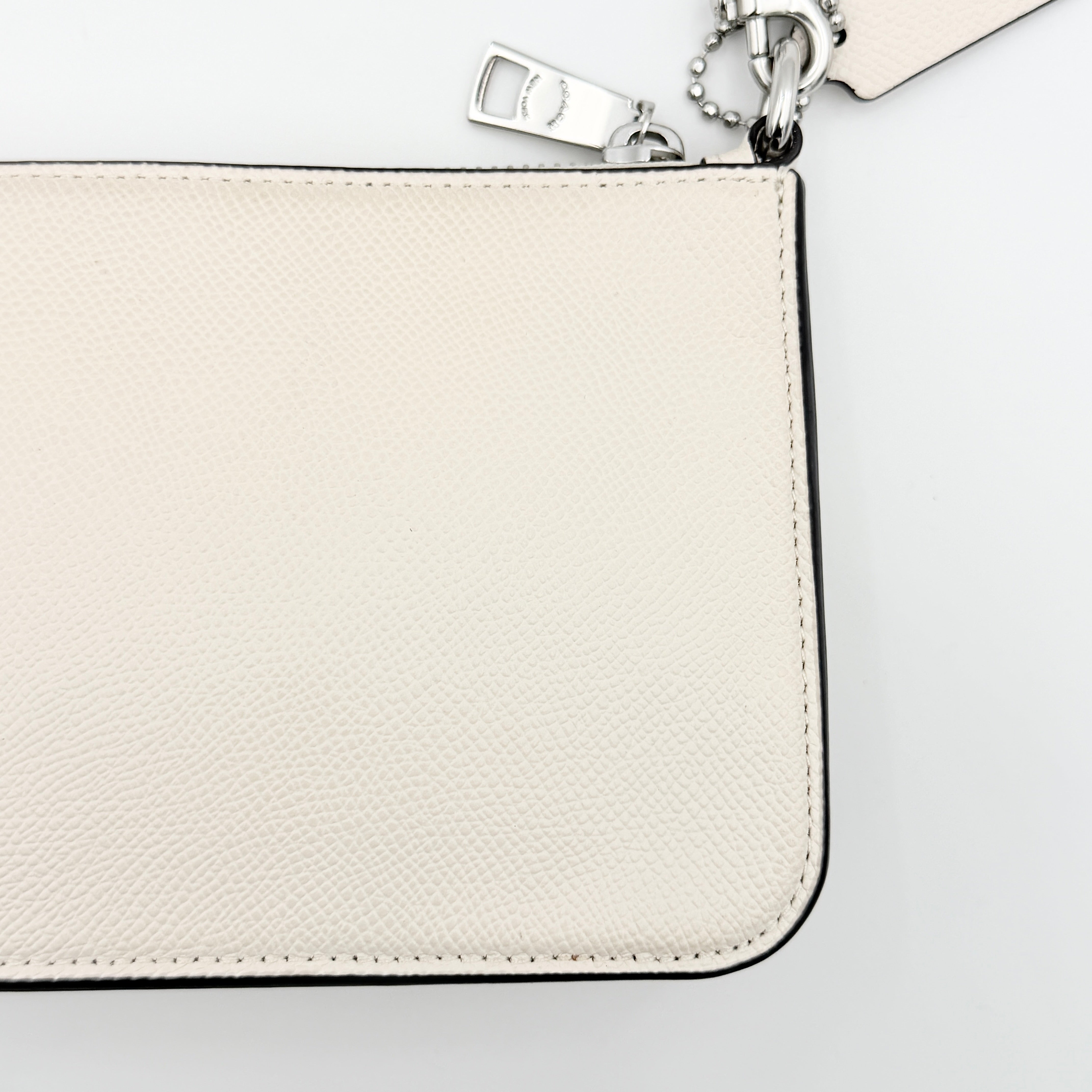 Coach cream grained leather shoulder bag with silver logo plaque and structured handle, displayed against a white background.