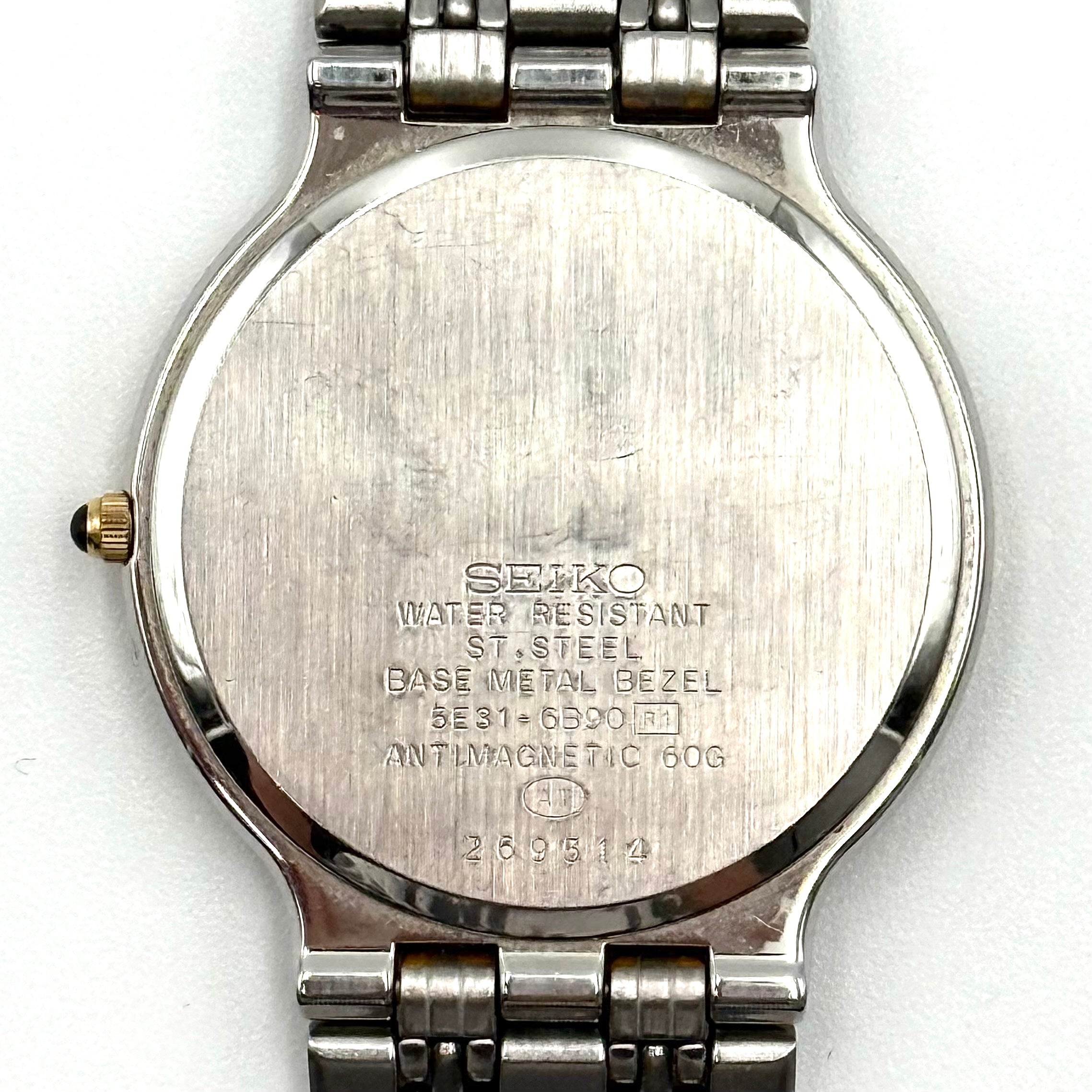 Seiko Dolce 5E31-6B90 watch in stainless steel with gold-tone accents and a cream dial, displayed on a black cushion.