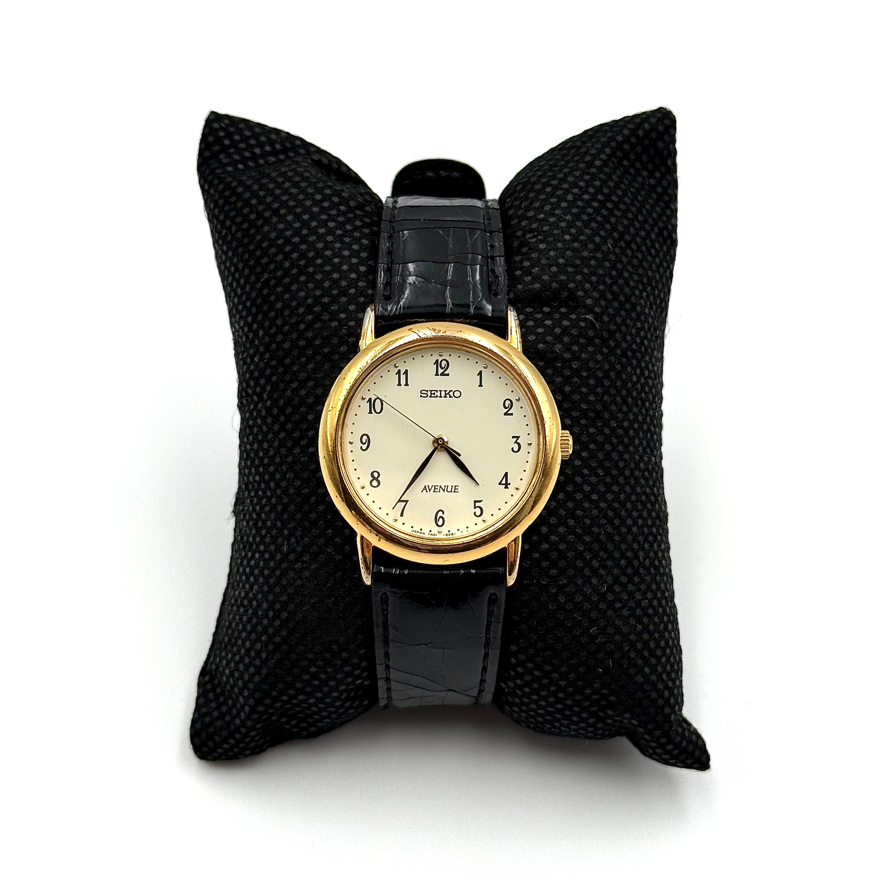 Seiko Avenue 7N01-6D50 gold watch with black textured leather strap displayed on a black cushion.