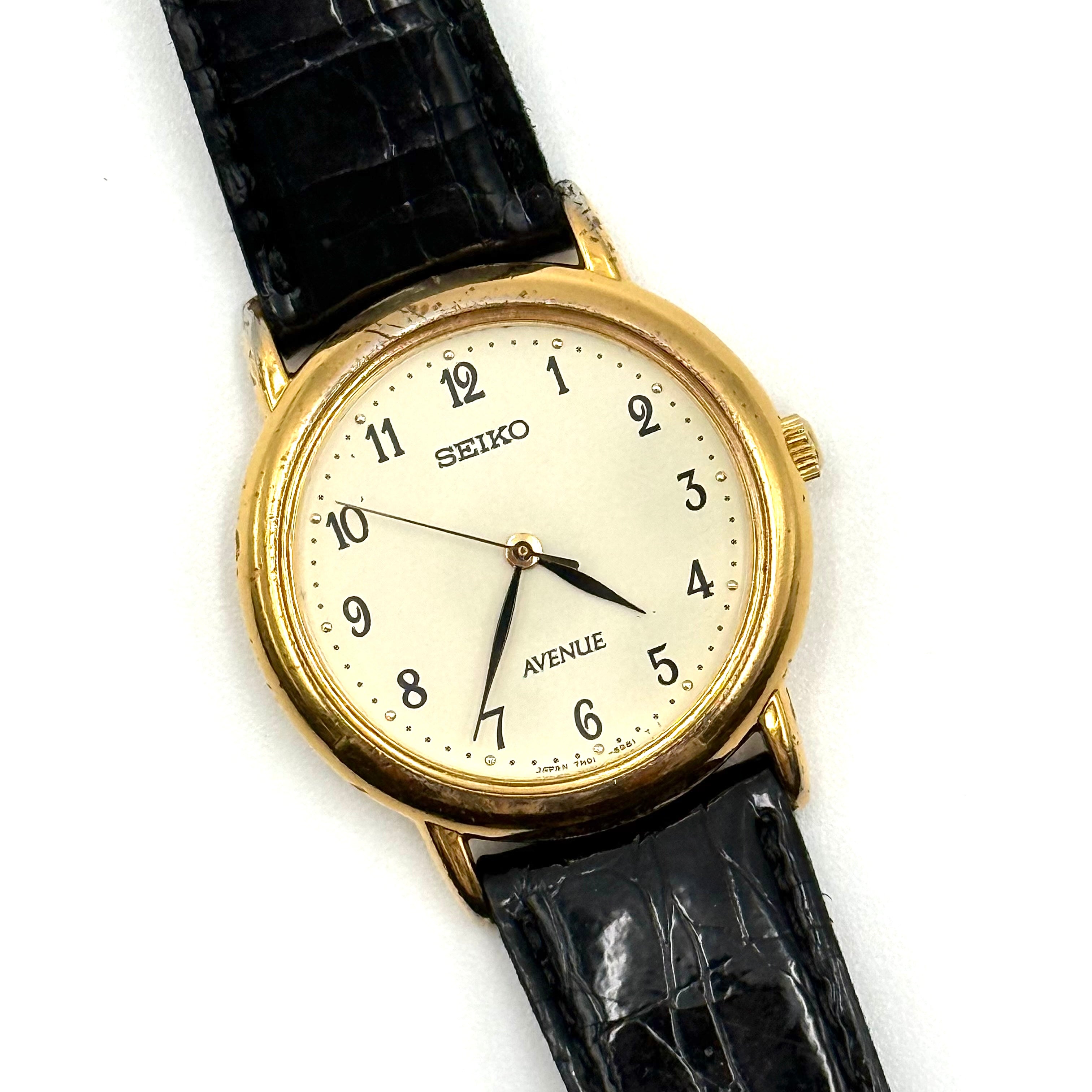 Seiko Avenue 7N01-6D50 gold watch with black textured leather strap displayed on a black cushion.