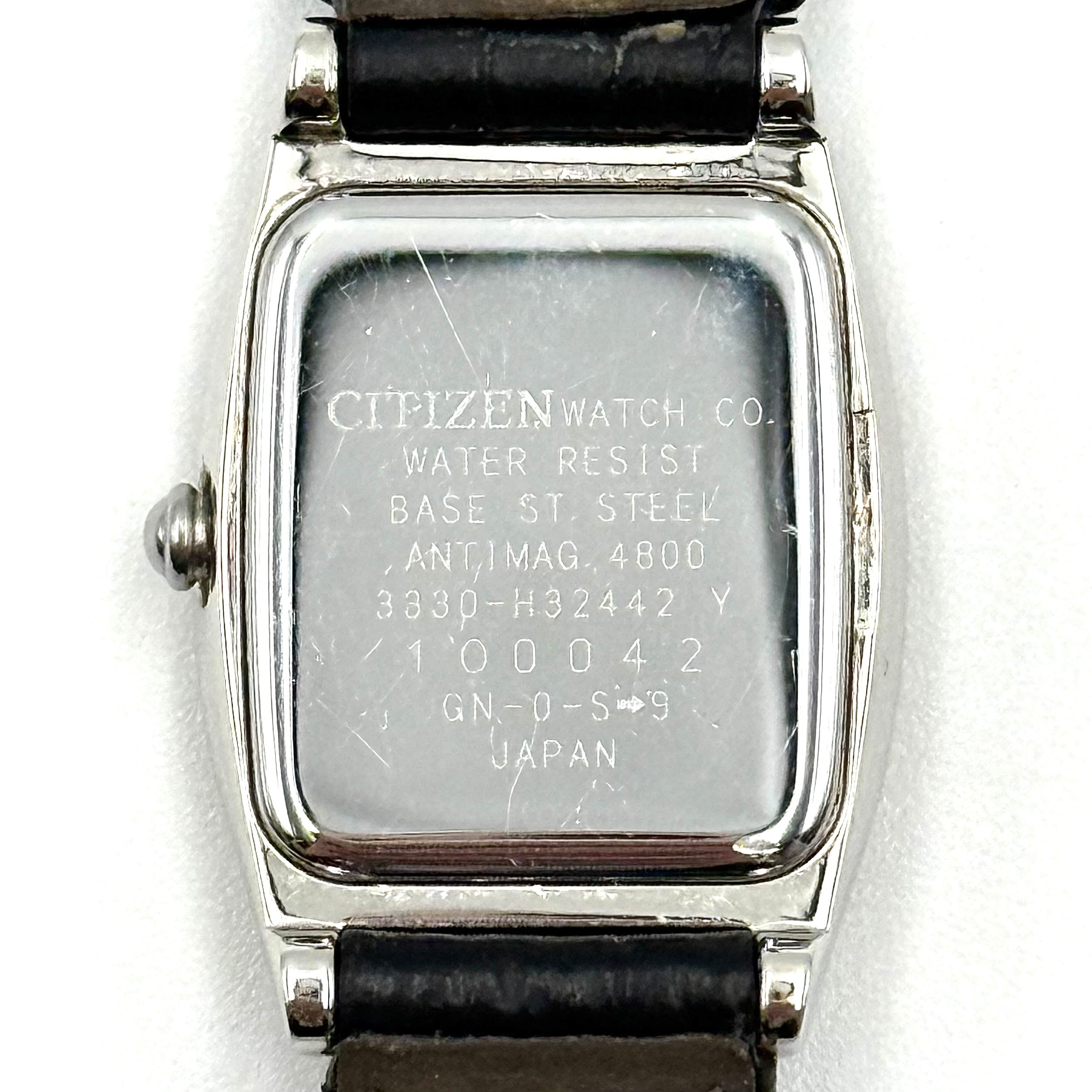 Citizen Exceed watch featuring a dark blue dial, tonneau-shaped stainless steel case, and black leather strap displayed on a black cushion.