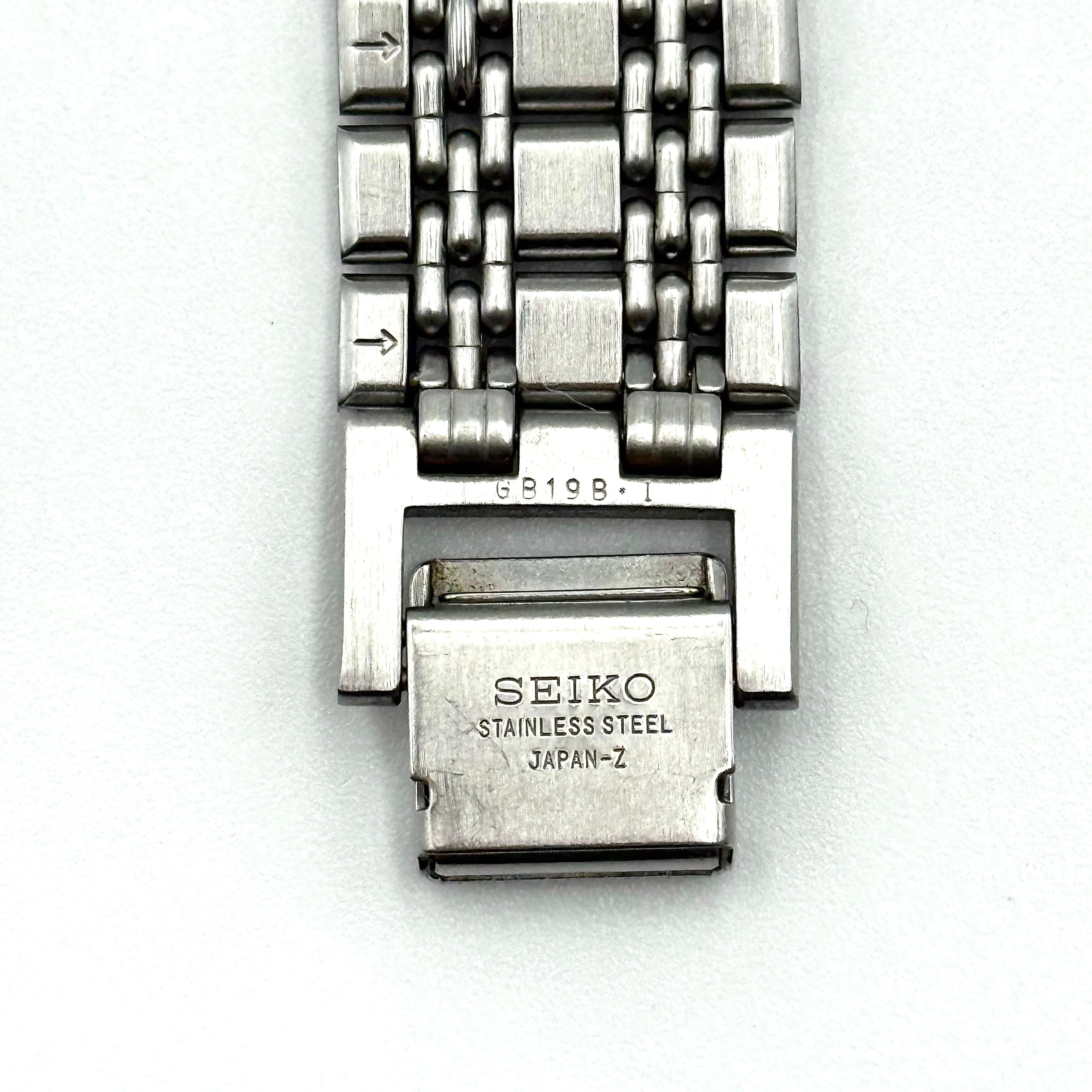 Seiko Dolce 5E31-6B90 watch in stainless steel with gold-tone accents and a cream dial, displayed on a black cushion.