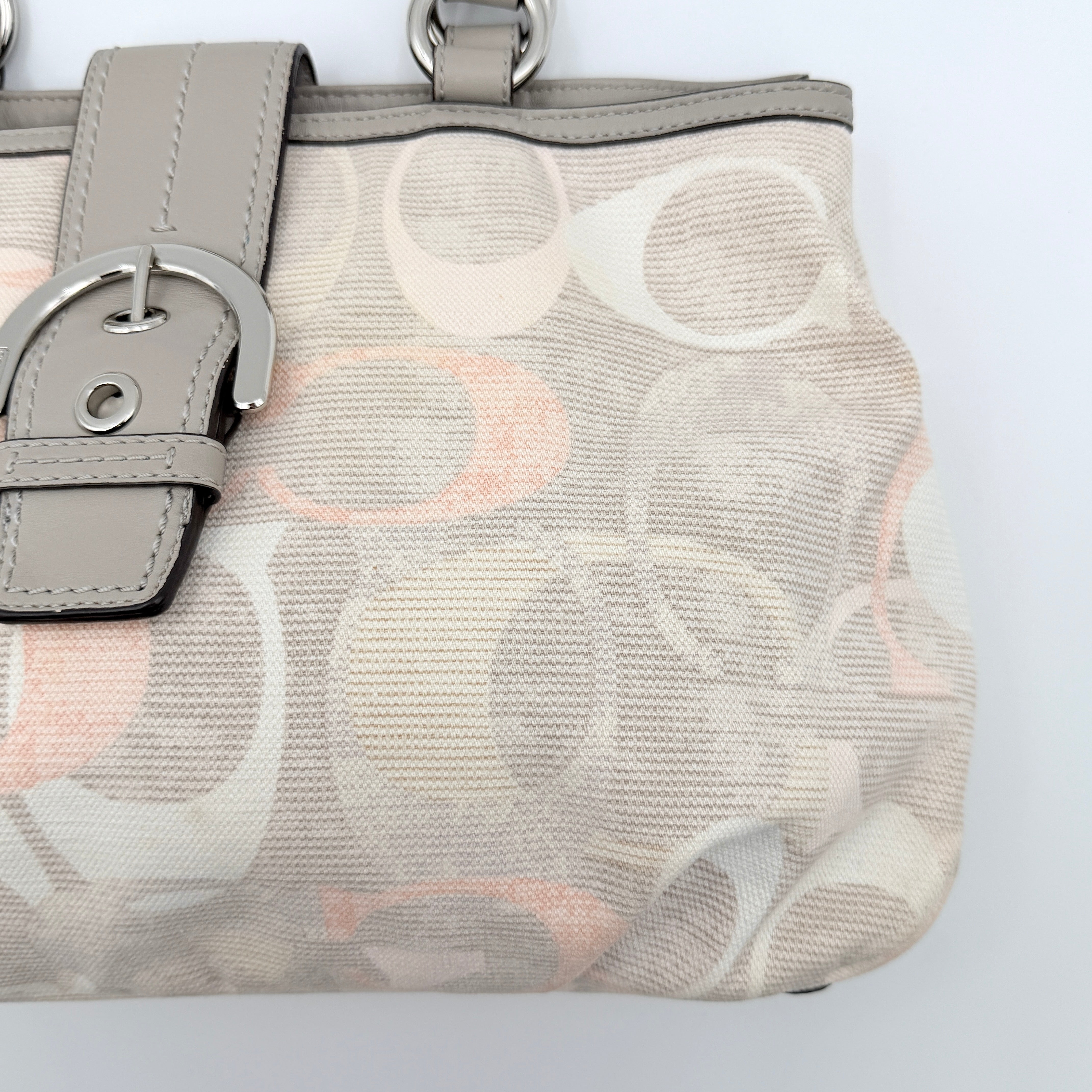 Coach Signature Optic Soho Shoulder Bag in grey and pink canvas with leather handles and buckle detail, shown against a white background.