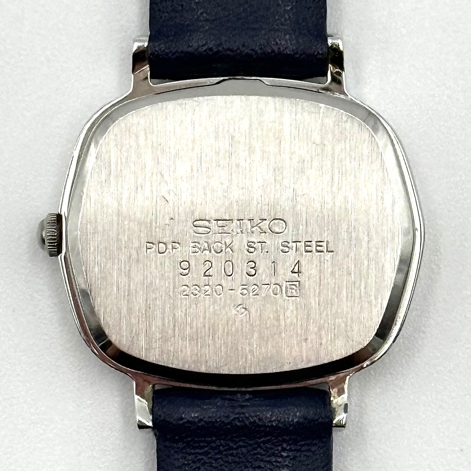 Seiko Quartz 2320-5270 with a square stainless steel case, copper dial, and navy blue leather strap displayed on a textured cushion.
