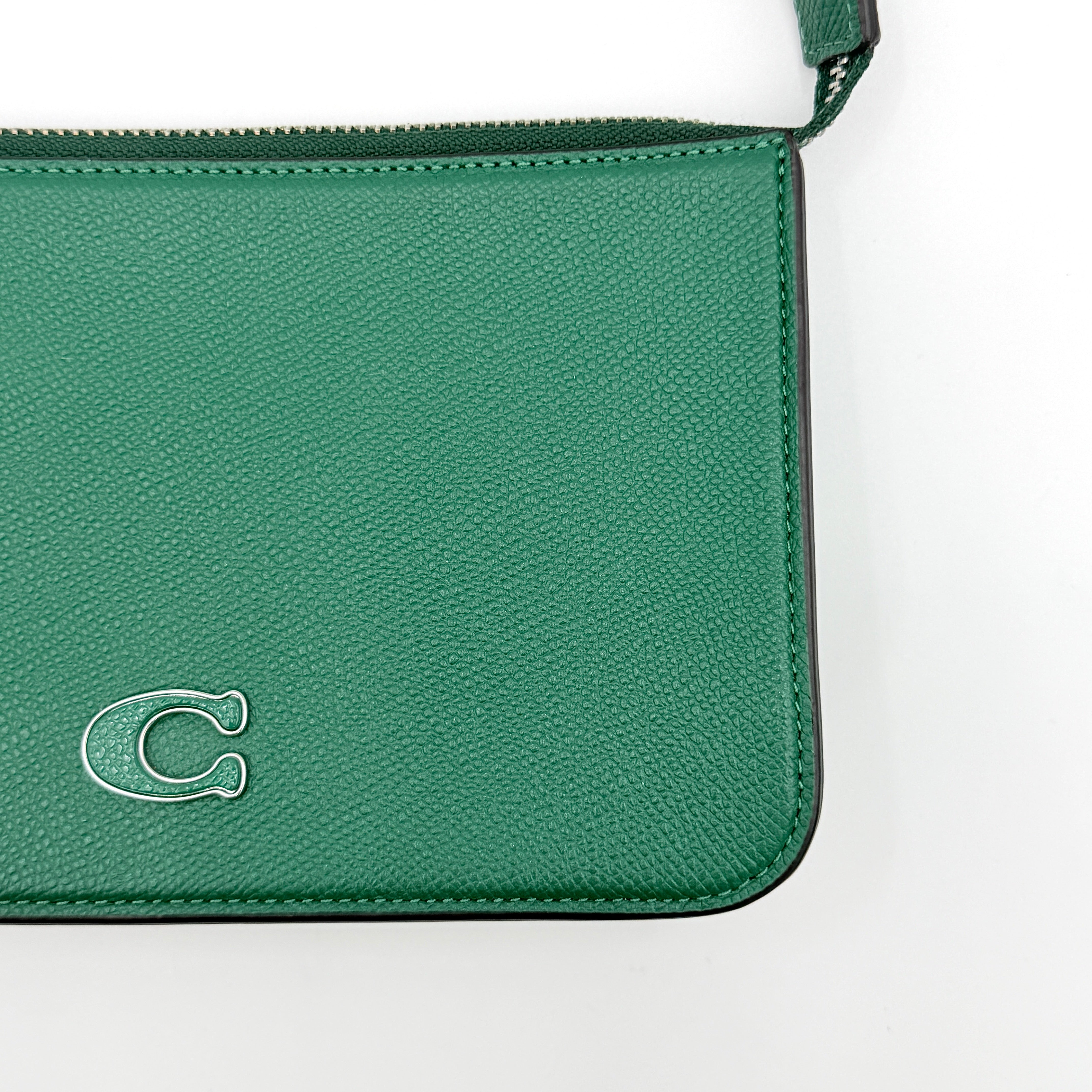 Coach green grained leather shoulder bag with silver C plaque and top zip, styled with a short strap.
