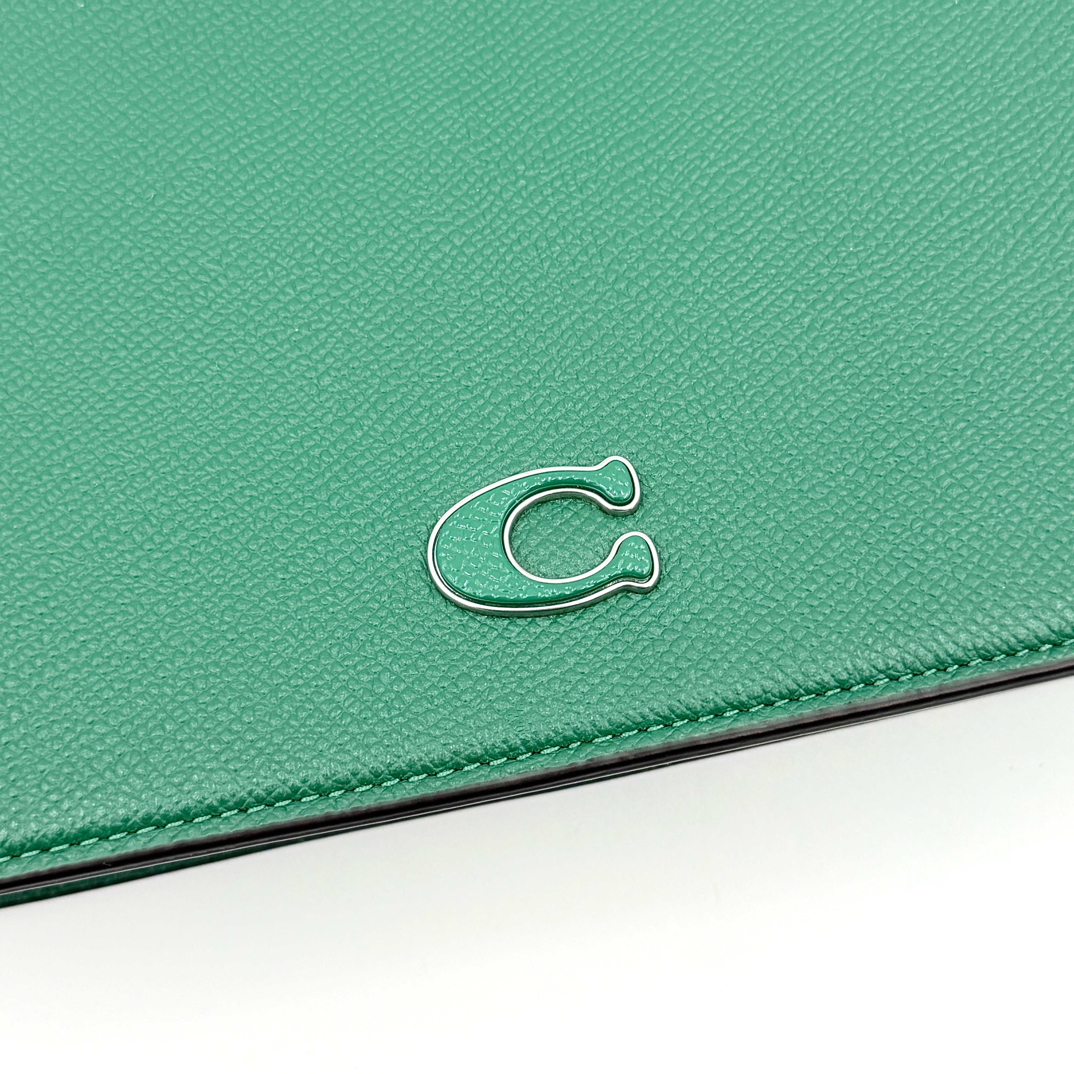 Coach green grained leather shoulder bag with silver C plaque and top zip, styled with a short strap.