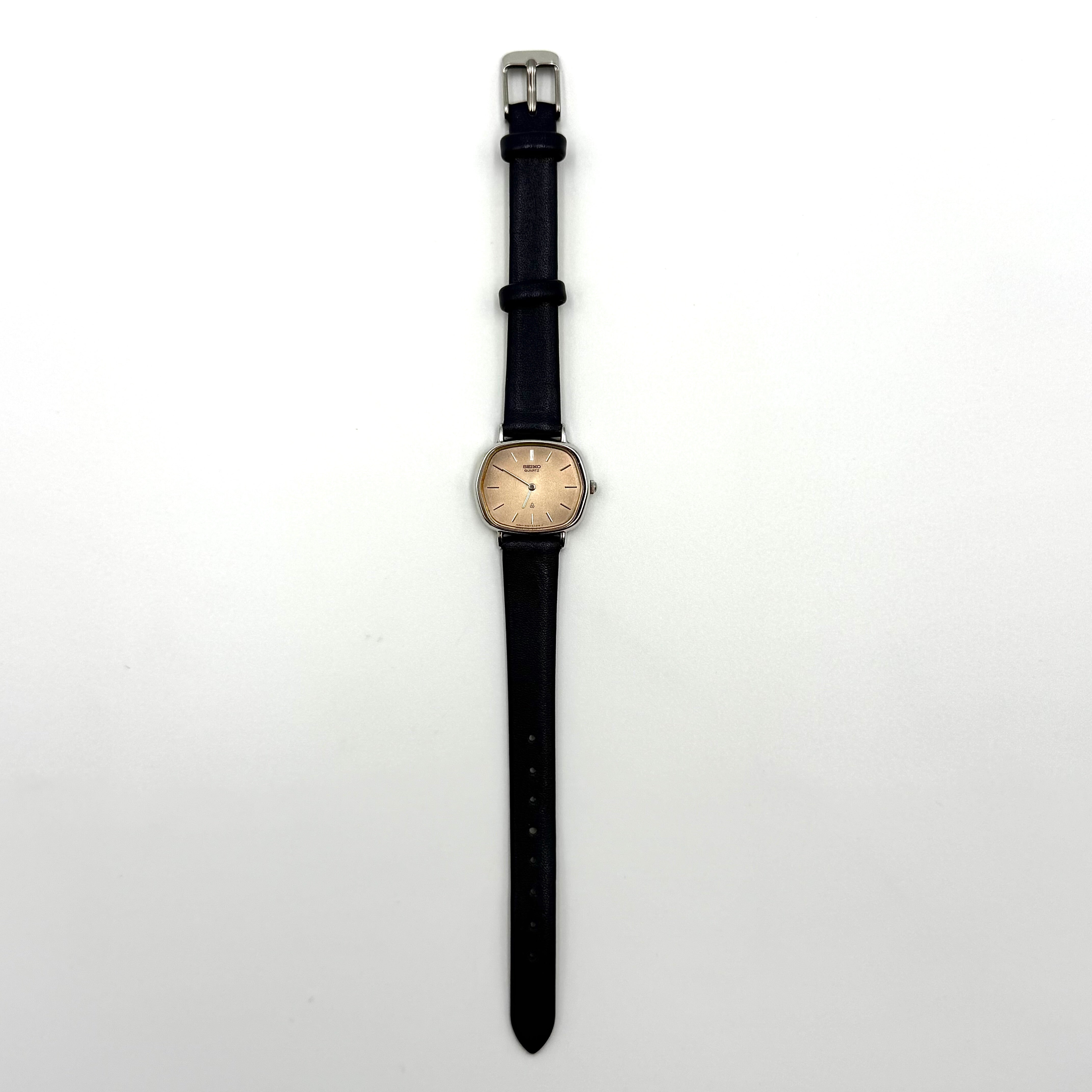 Seiko Quartz 2320-5270 with a square stainless steel case, copper dial, and navy blue leather strap displayed on a textured cushion.