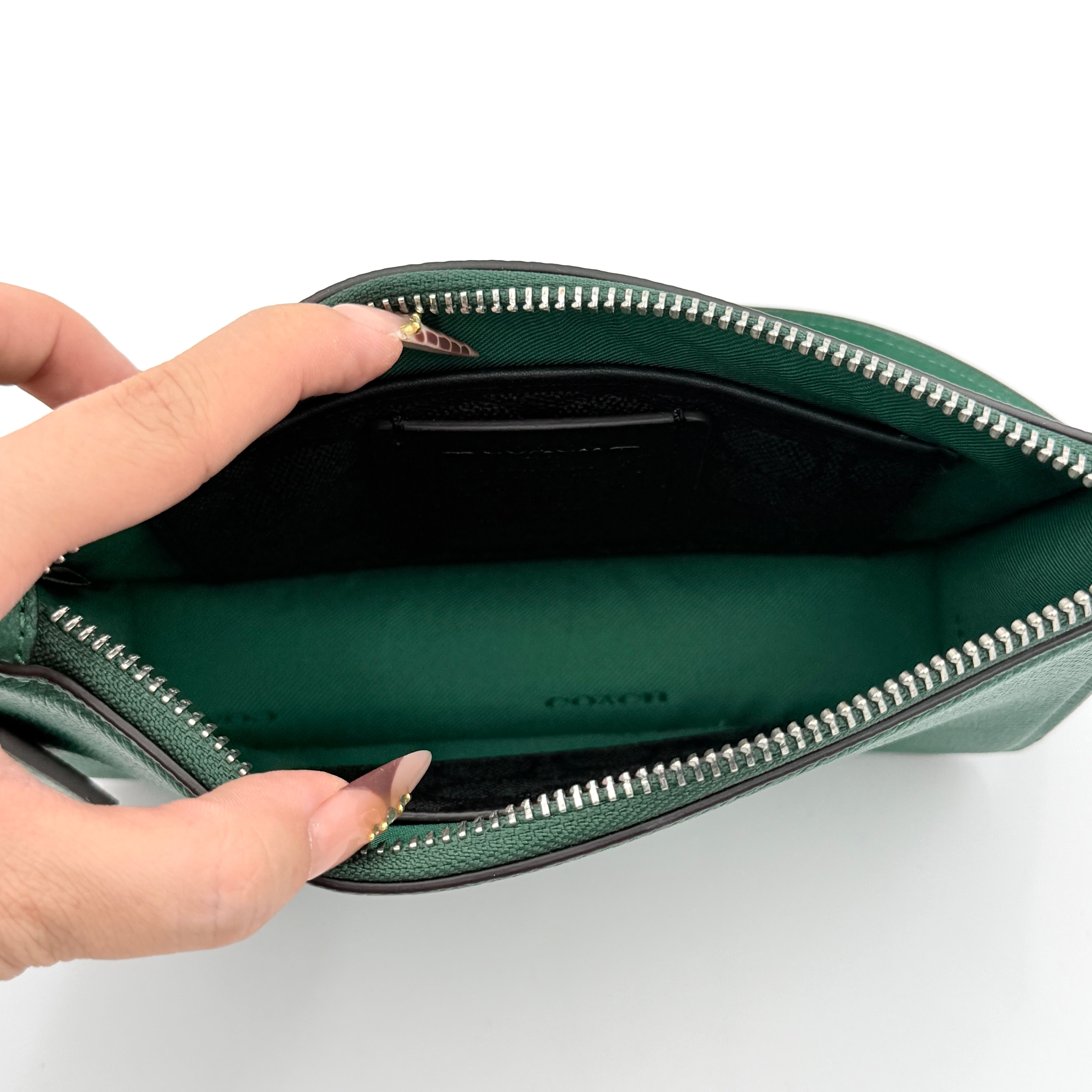 Coach green grained leather shoulder bag with silver C plaque and top zip, styled with a short strap.