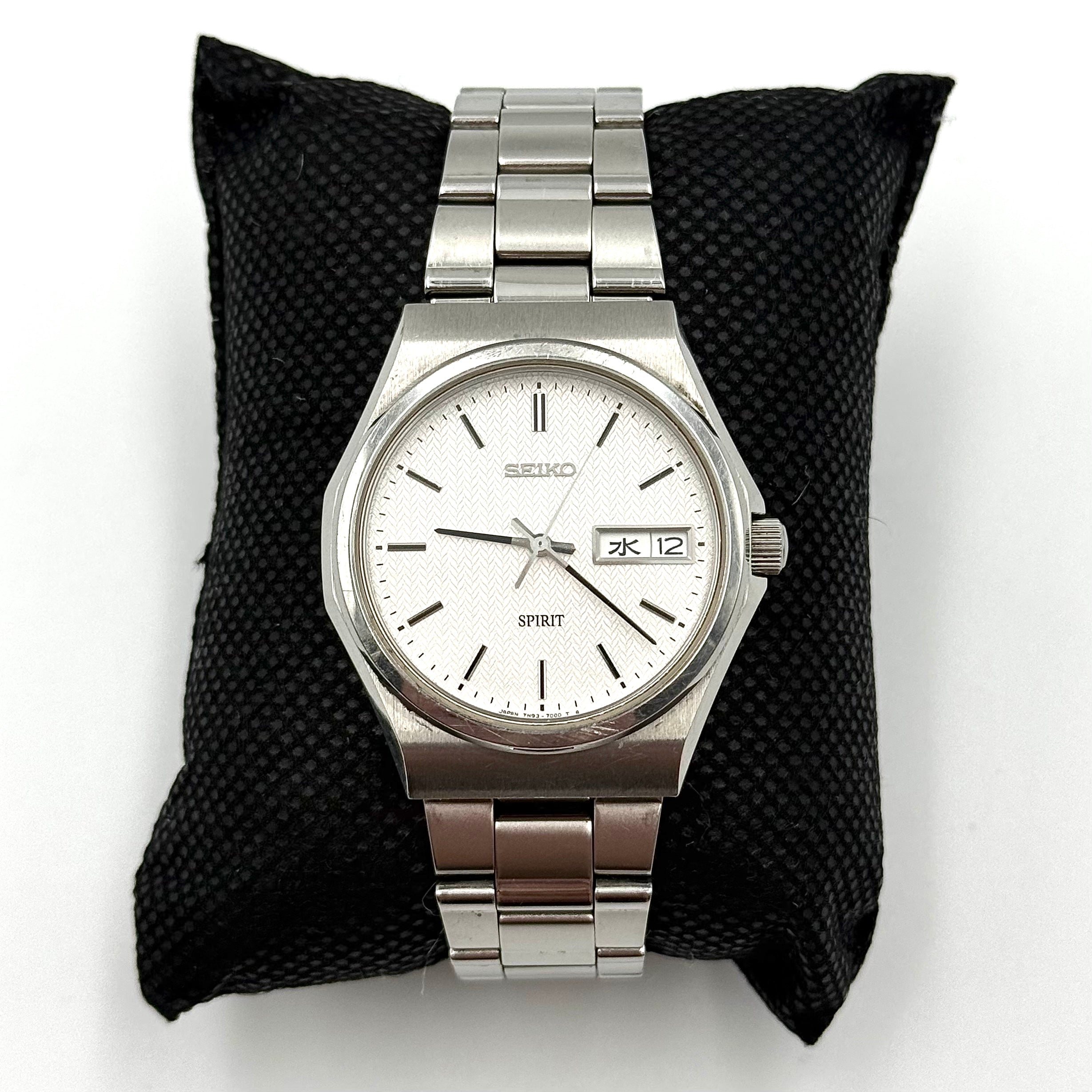 Seiko Spirit 7N93-7000 Quartz Watch in silver with a white textured dial and stainless steel bracelet, shown on a black cushion.