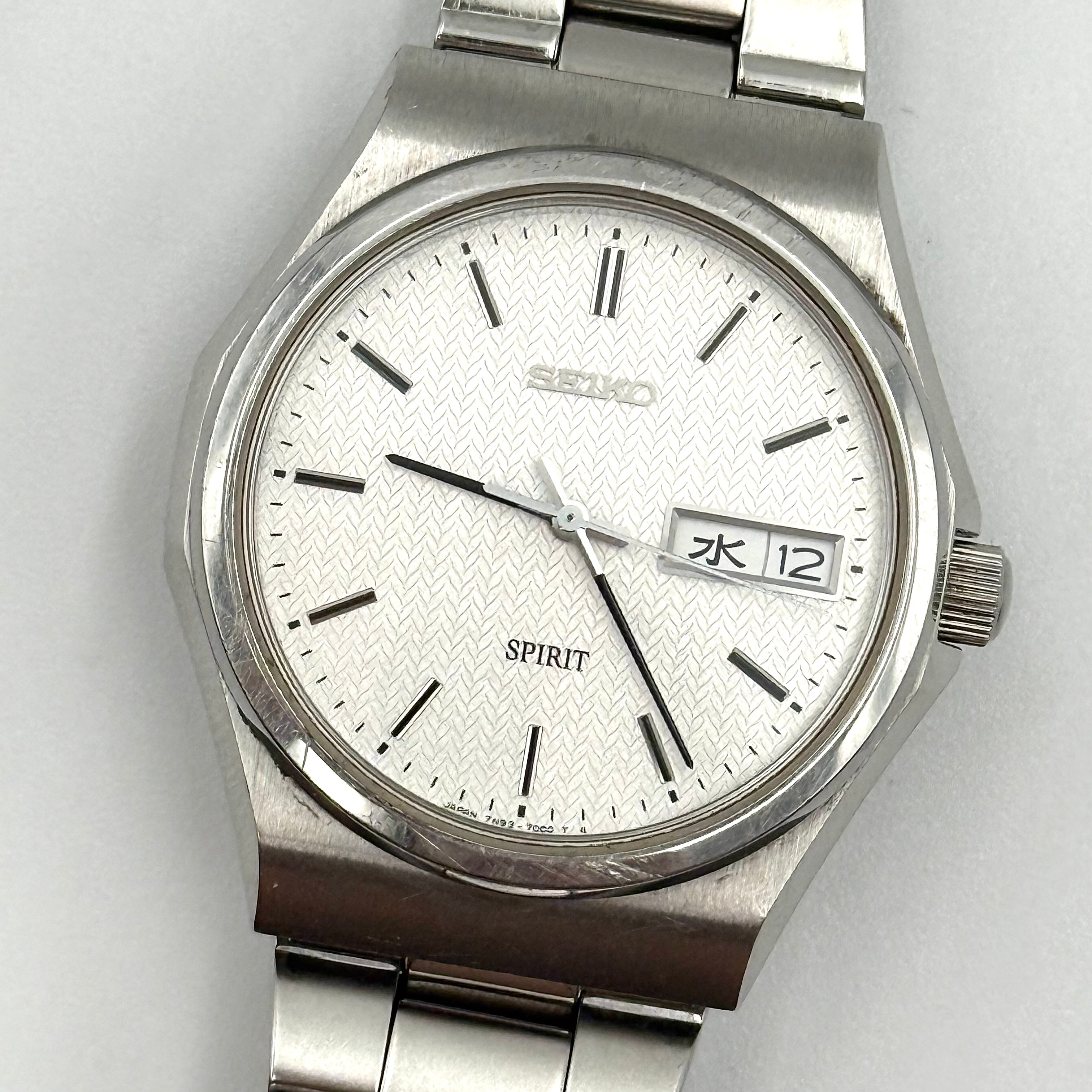 Seiko Spirit 7N93-7000 Quartz Watch in silver with a white textured dial and stainless steel bracelet, shown on a black cushion.