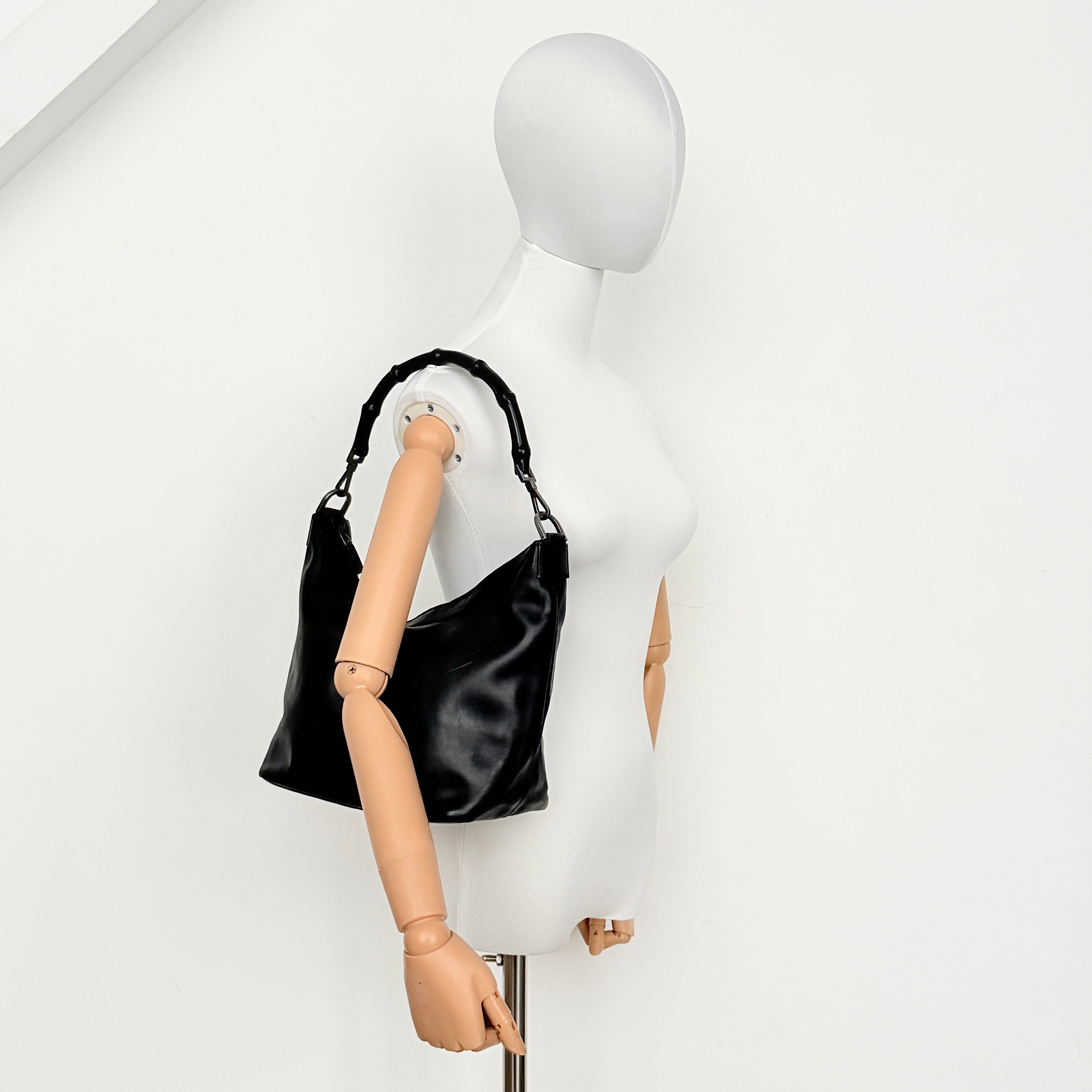 Gucci black leather hobo bag with bamboo handle and silver-tone hardware shown against a white background.