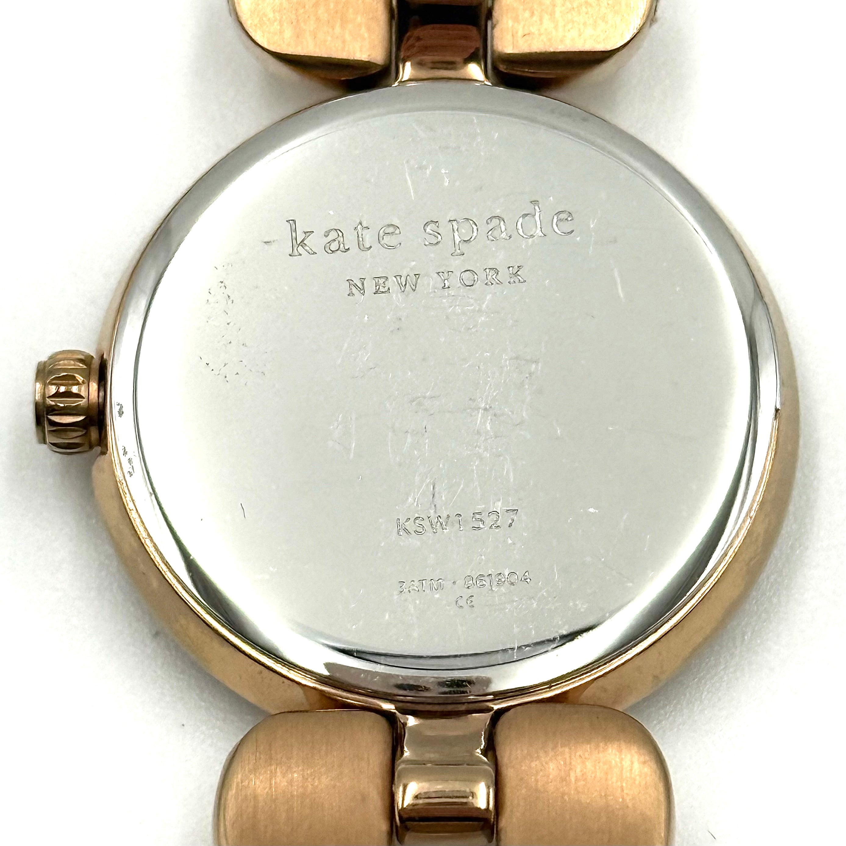Kate Spade Annadale gold bracelet watch with white dial and heart-shaped links displayed on a black cushion.