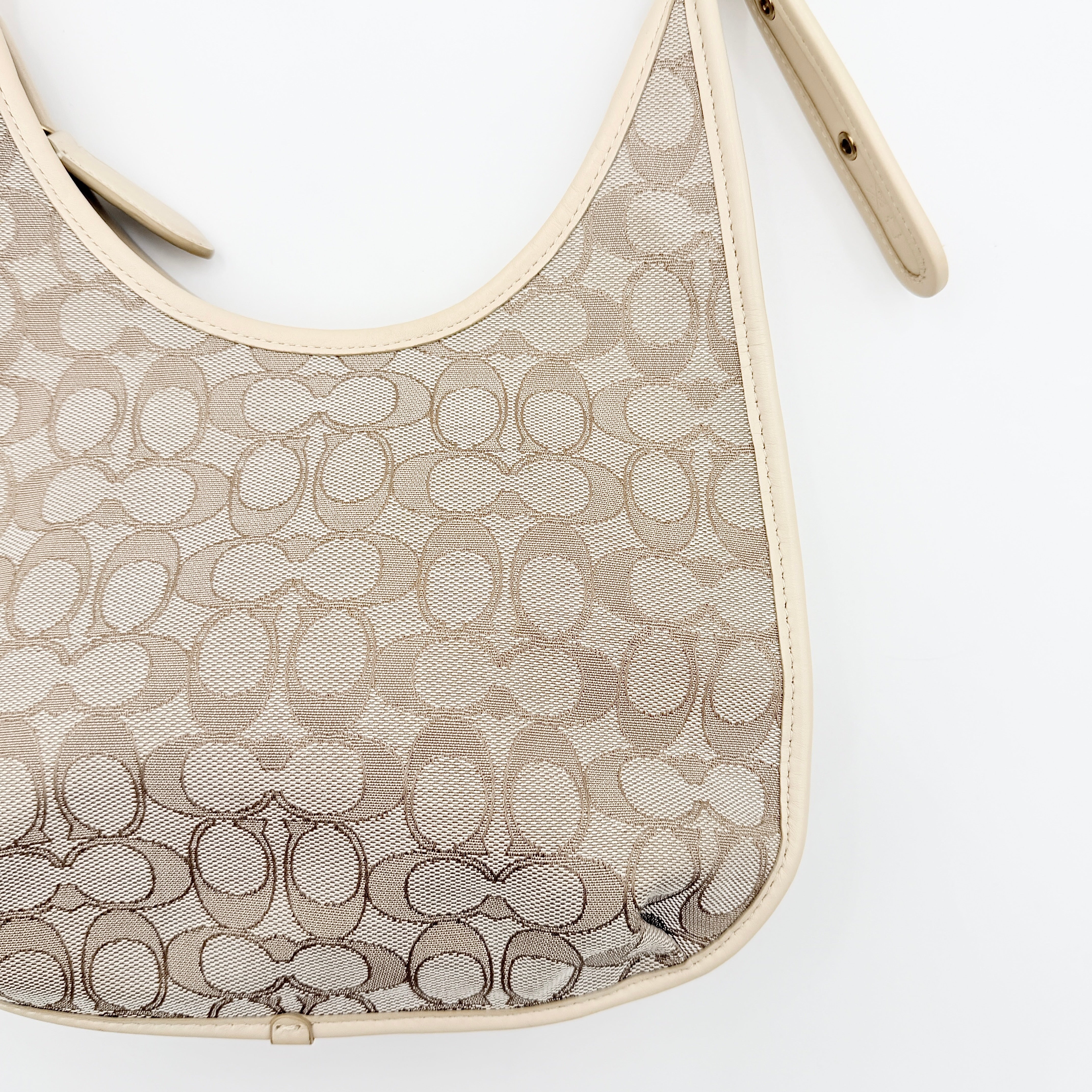 Coach Signature Ergo Shoulder Bag in beige and cream canvas with cream leather trim and brass adjustable buckle, displayed on a white background.