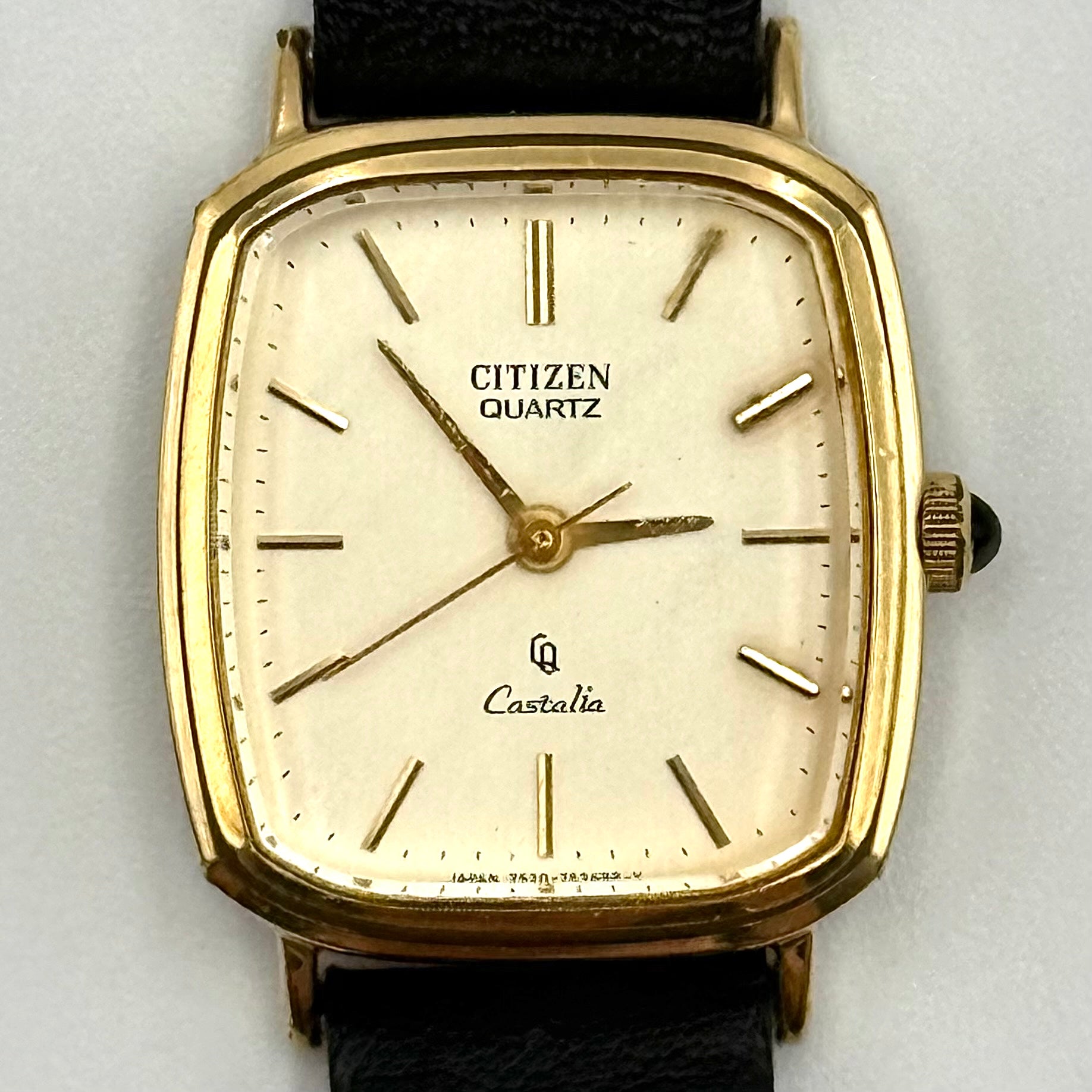 Citizen Castalia gold-tone square quartz watch with a champagne dial and black leather strap displayed on a black cushion.