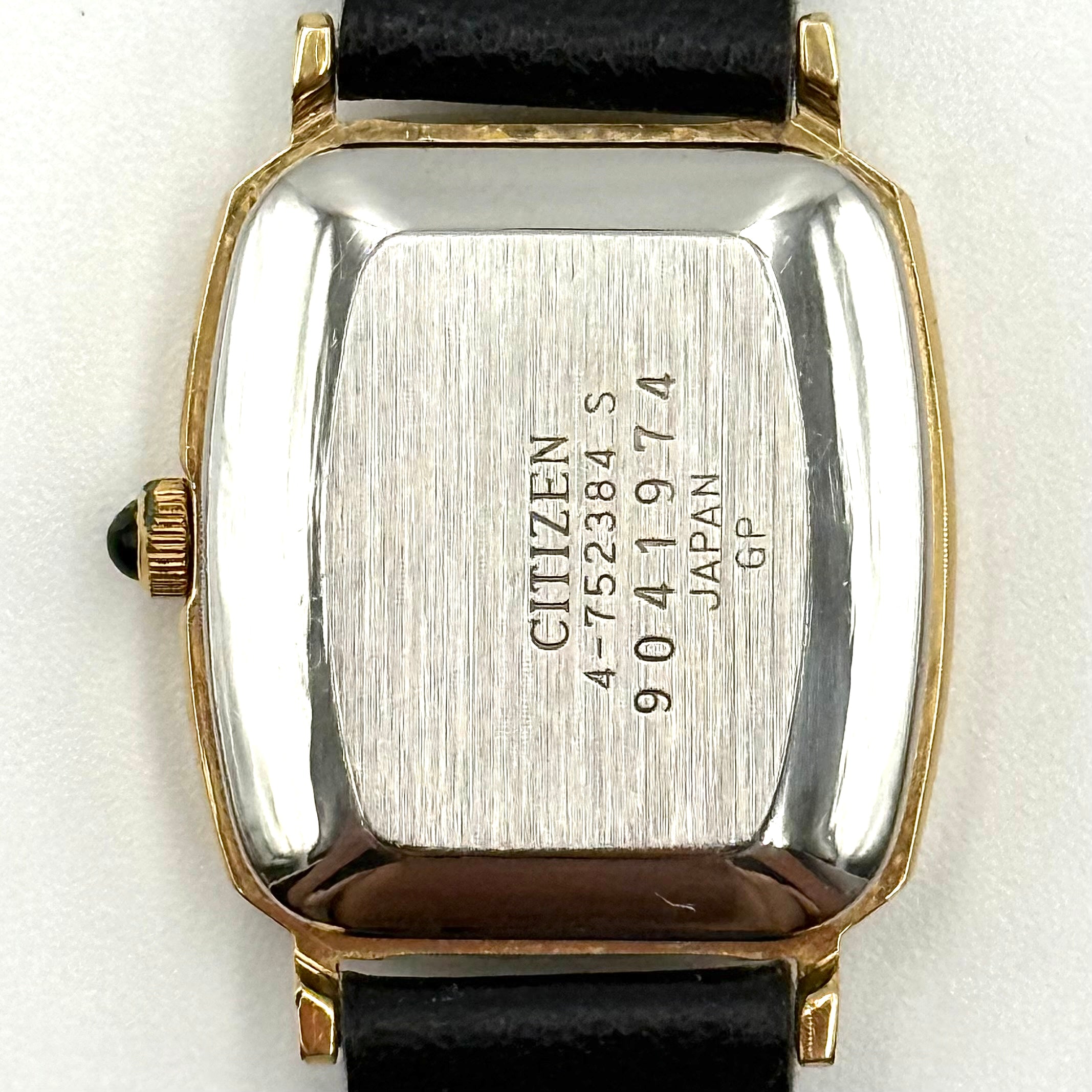 Citizen Castalia gold-tone square quartz watch with a champagne dial and black leather strap displayed on a black cushion.
