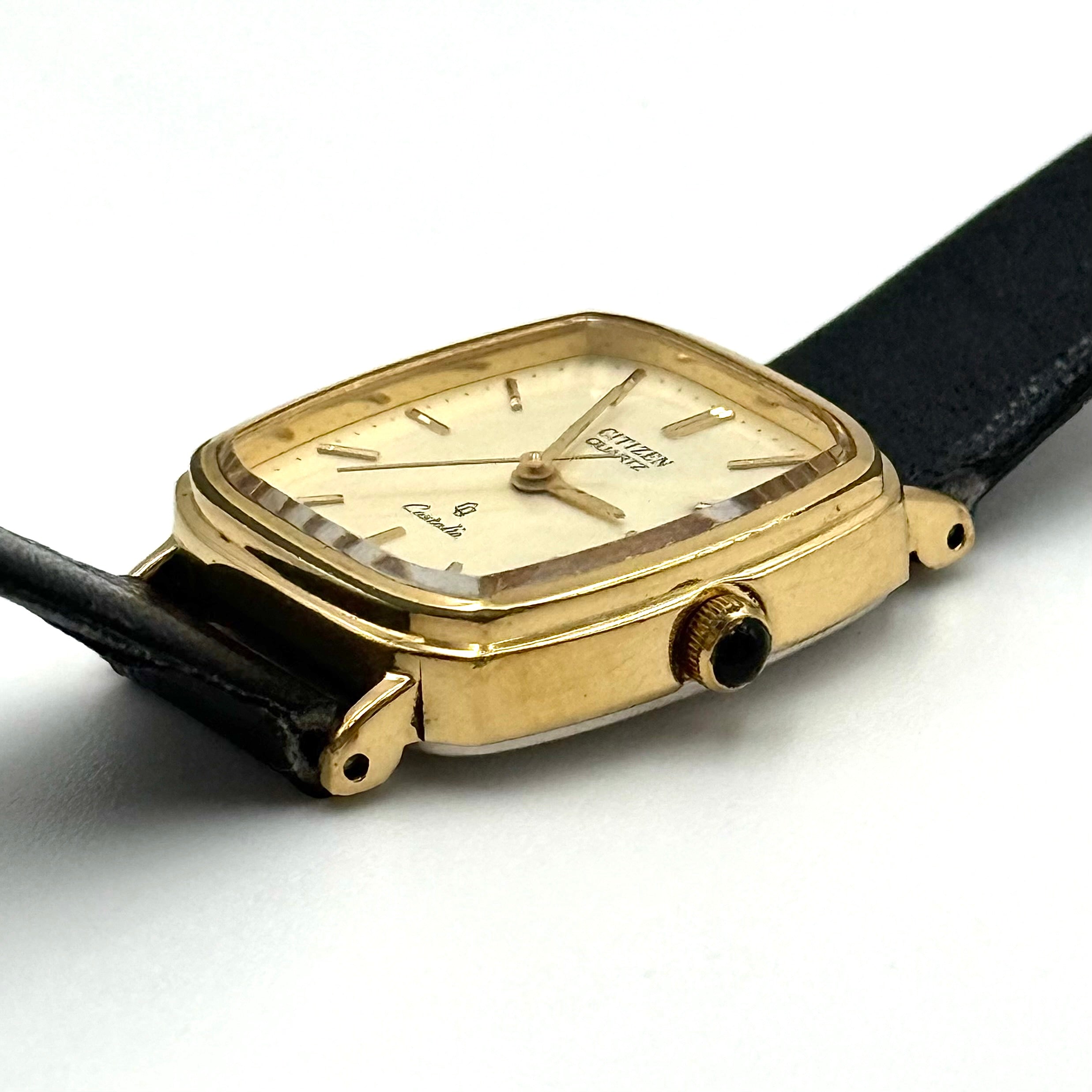 Citizen Castalia gold-tone square quartz watch with a champagne dial and black leather strap displayed on a black cushion.