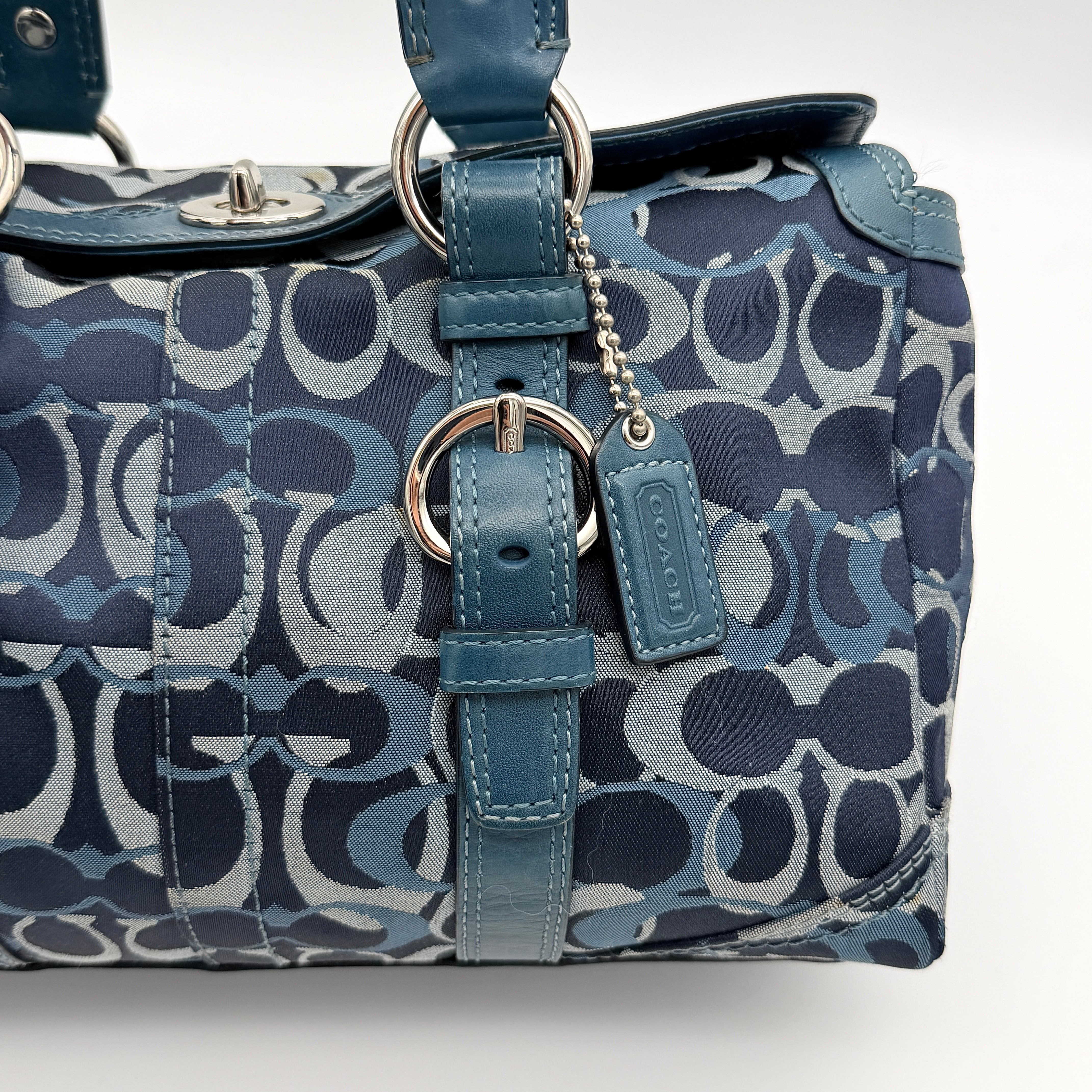 Coach Signature Chelsea Optic Satchel in blue canvas with leather braided handles and silver hardware, displayed on a Coach dust bag.
