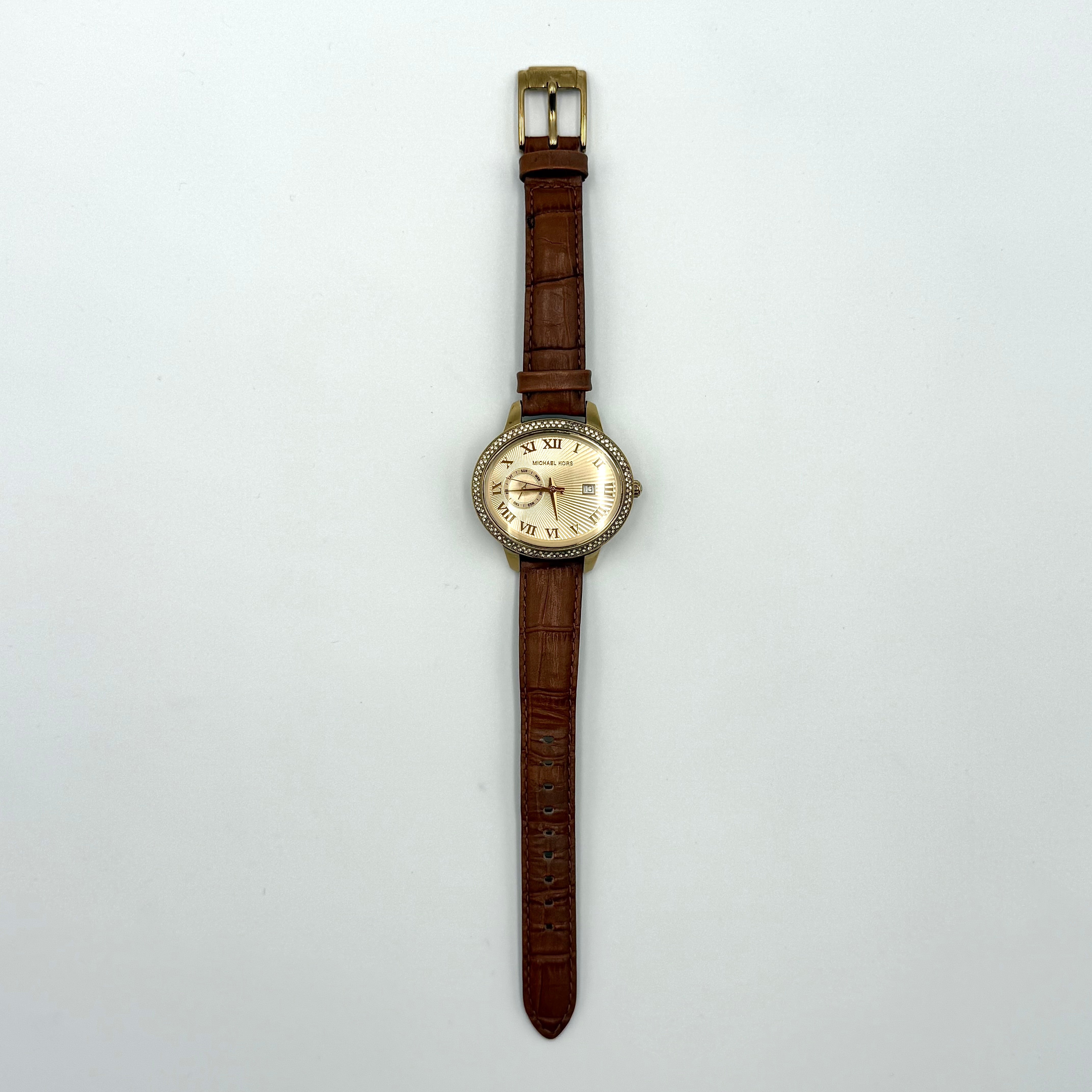 Michael Kors Whitley MK2428 watch with gold dial, crystal bezel and brown leather strap on black cushion