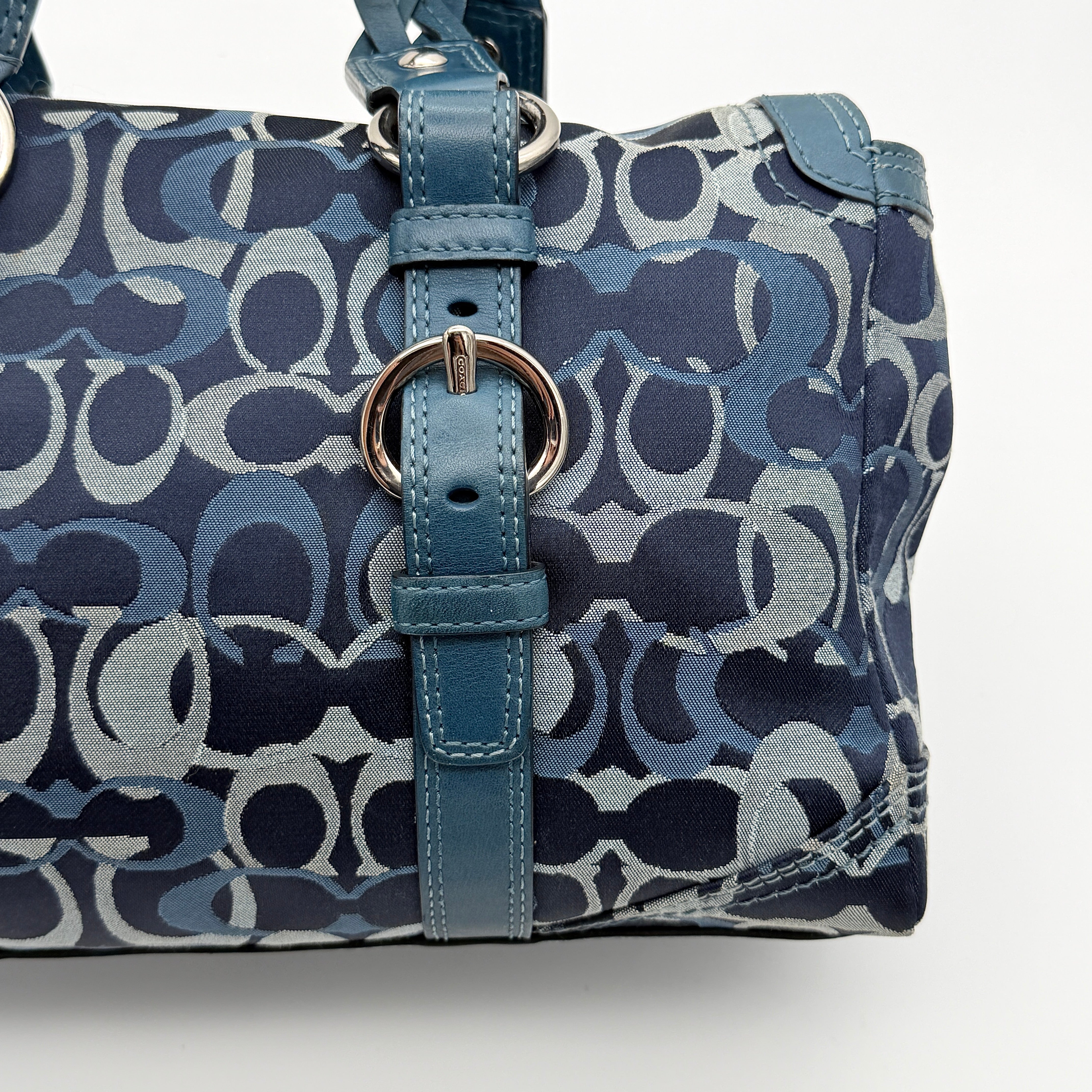 Coach Signature Chelsea Optic Satchel in blue canvas with leather braided handles and silver hardware, displayed on a Coach dust bag.