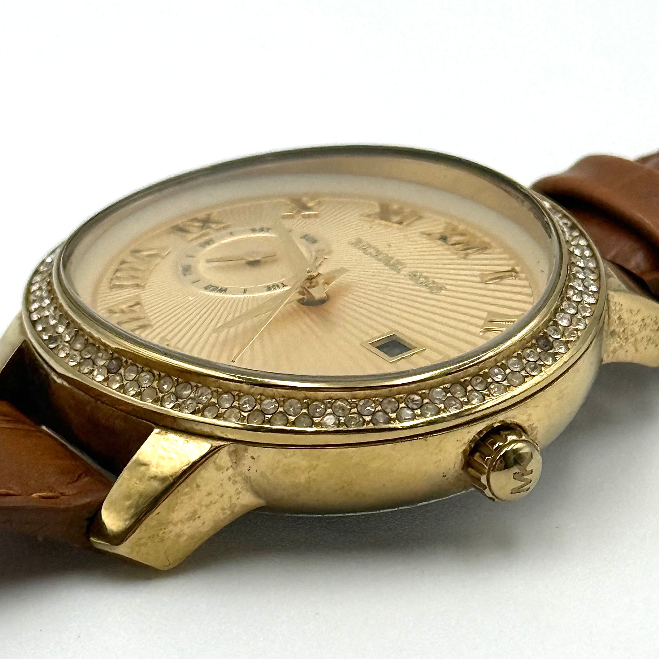 Michael Kors Whitley MK2428 watch with gold dial, crystal bezel and brown leather strap on black cushion
