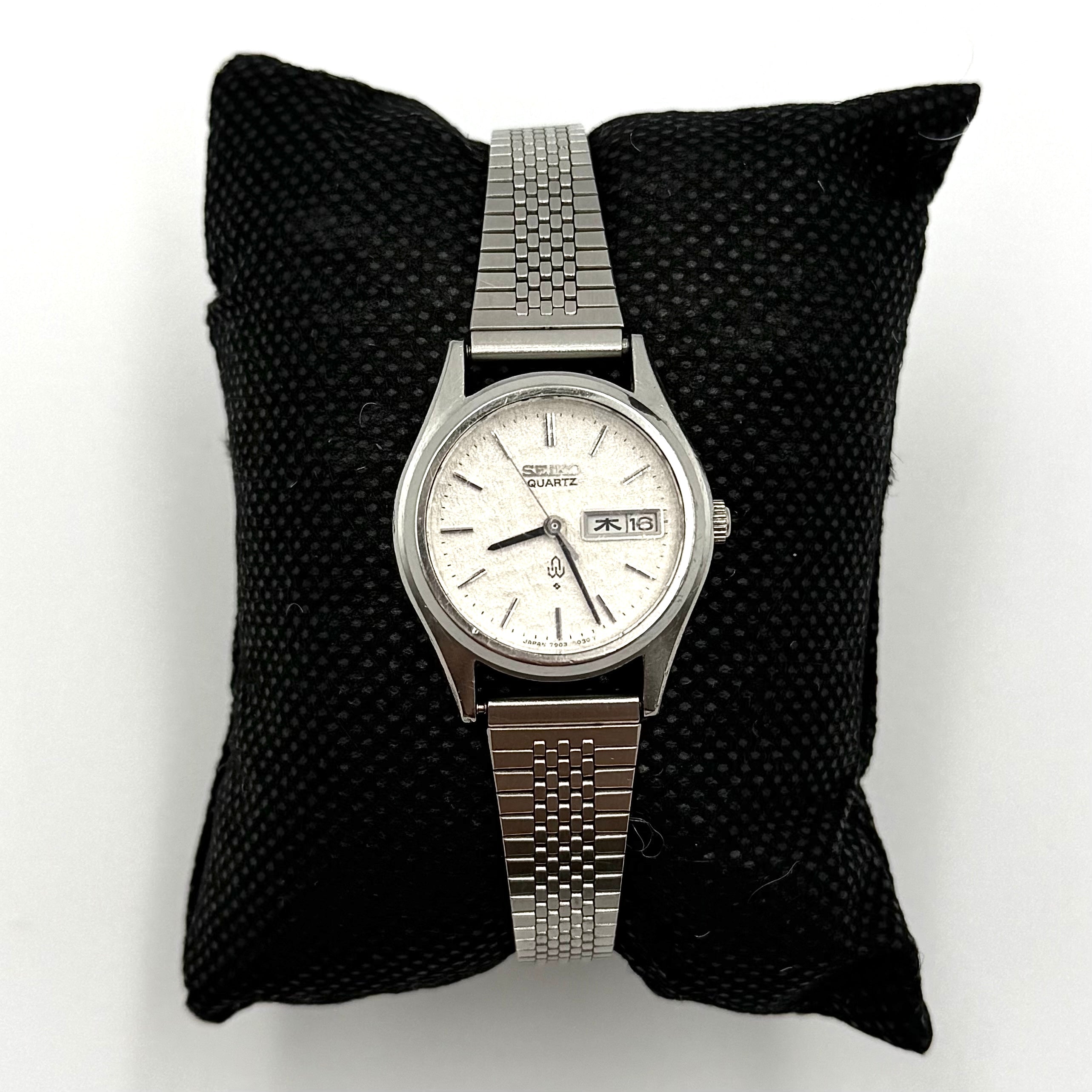 Seiko 7903-0030 Quartz stainless steel watch with a white textured dial and matching steel bracelet on a display pillow.