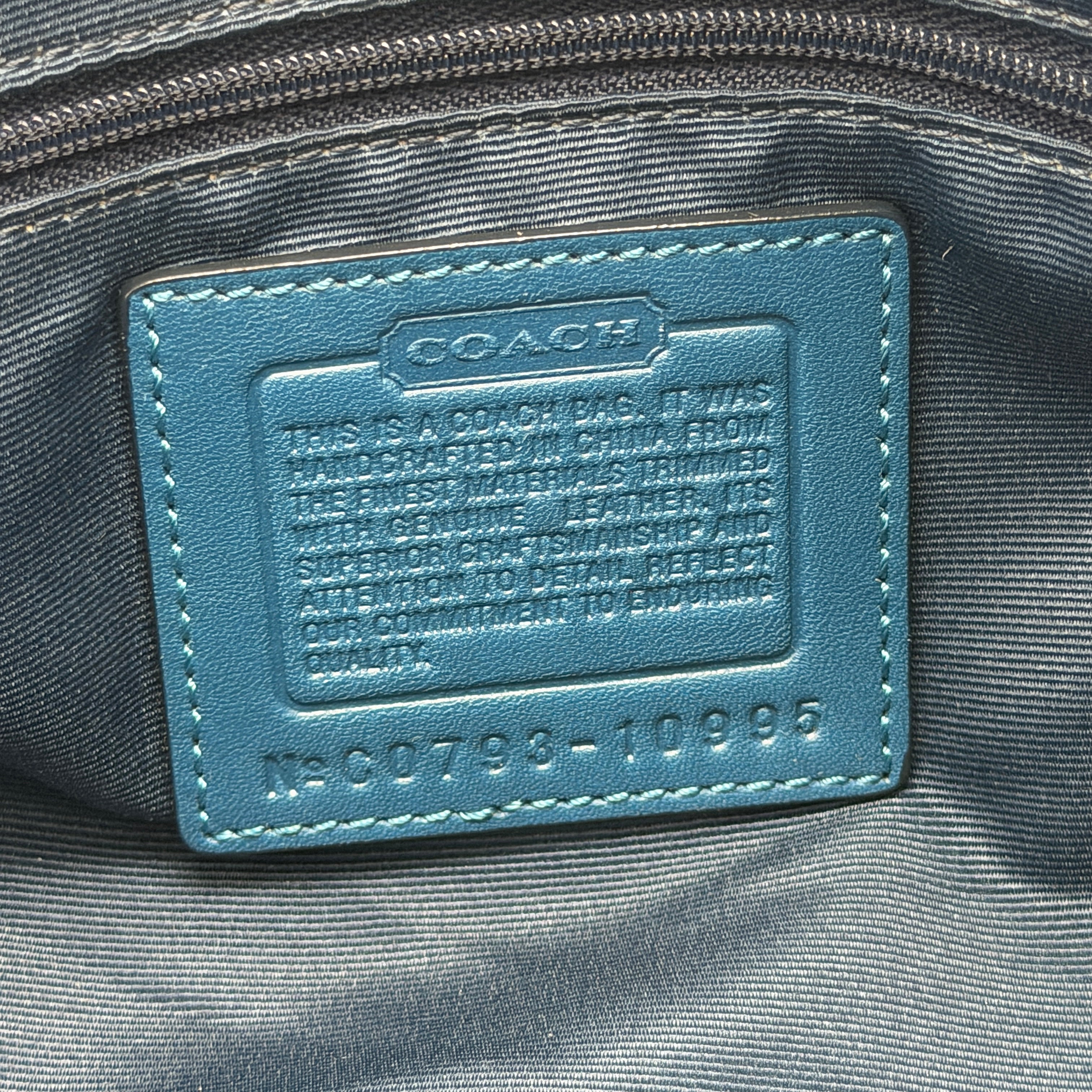 Coach Signature Chelsea Optic Satchel in blue canvas with leather braided handles and silver hardware, displayed on a Coach dust bag.