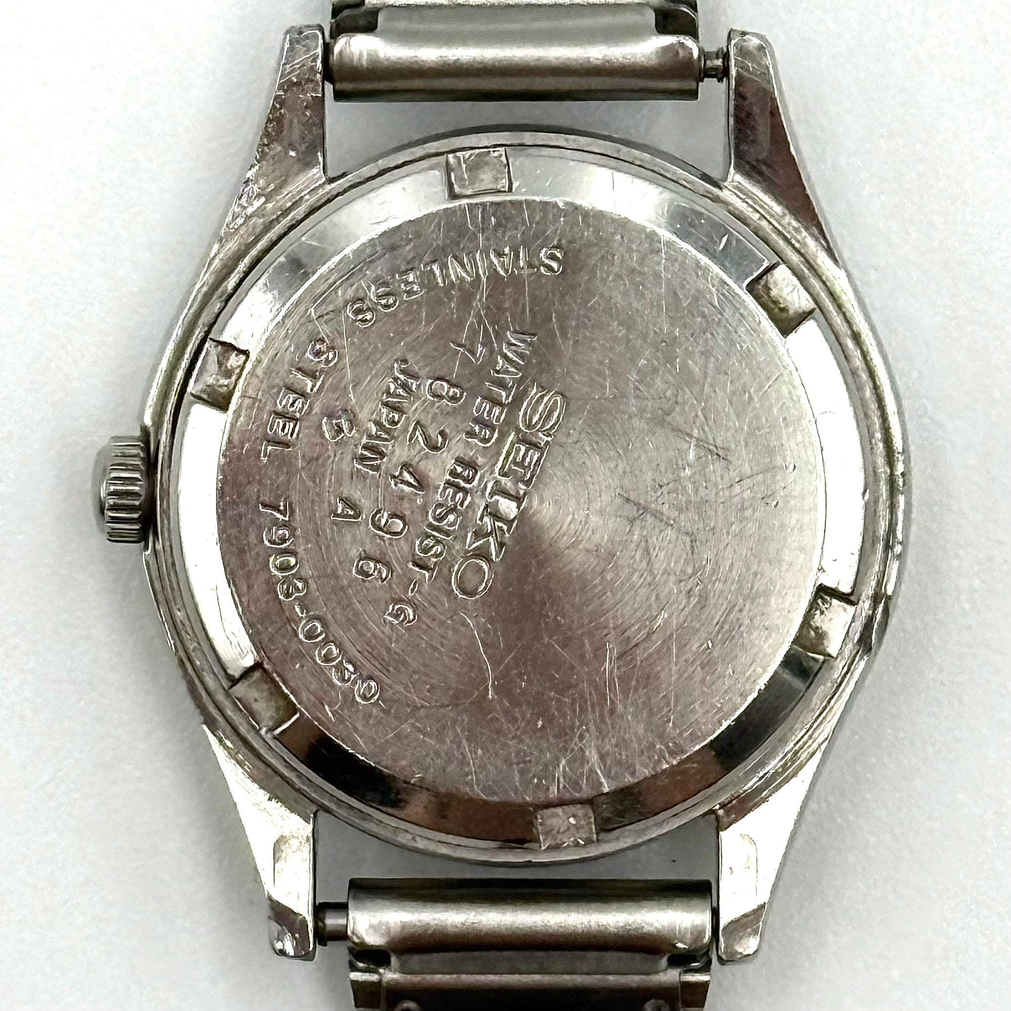 Seiko 7903-0030 Quartz stainless steel watch with a white textured dial and matching steel bracelet on a display pillow.