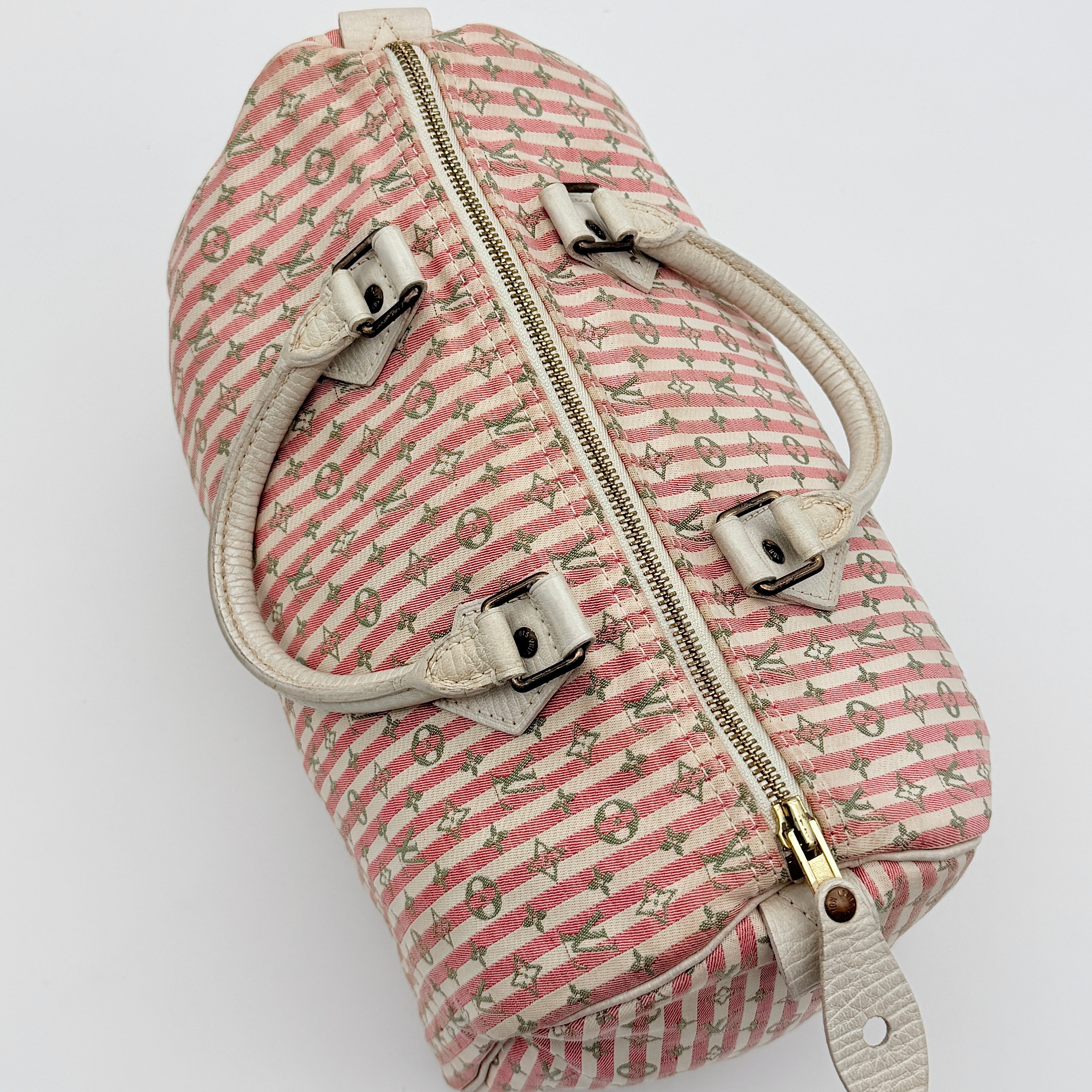 Louis Vuitton Speedy 30 in pink Mini Lin Monogram with cream leather handles and gold-tone zip, displayed on a neutral background.