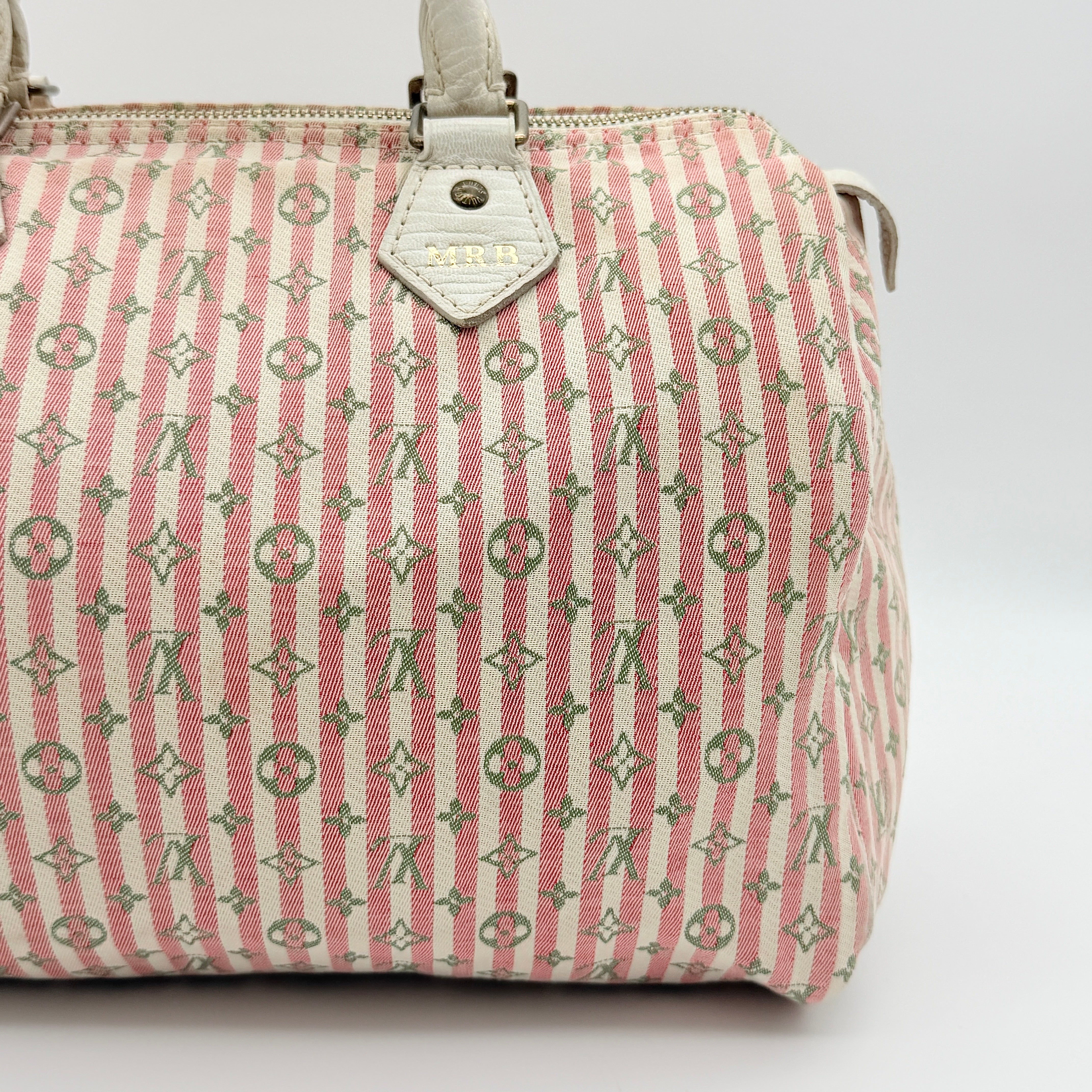 Louis Vuitton Speedy 30 in pink Mini Lin Monogram with cream leather handles and gold-tone zip, displayed on a neutral background.