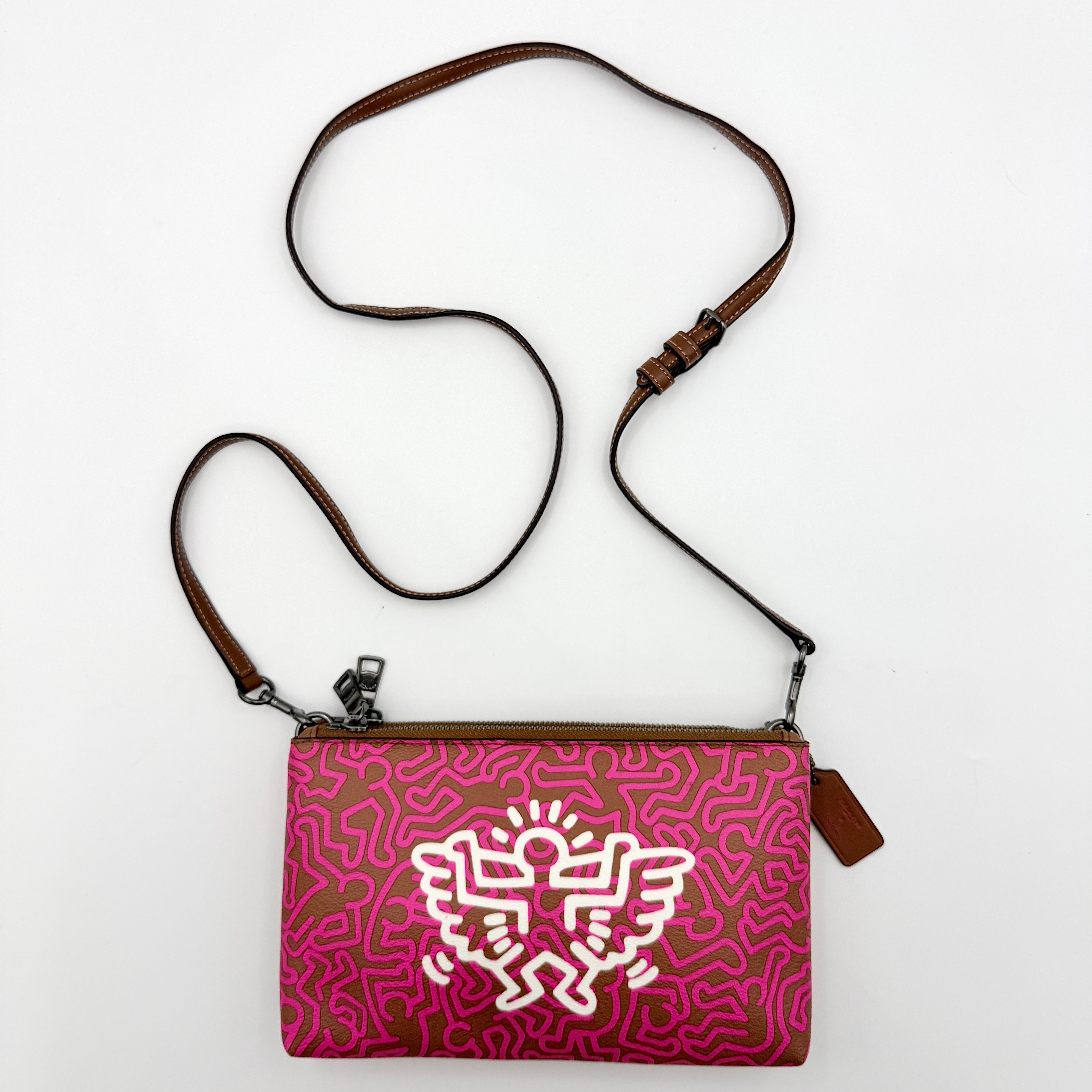 Coach x Keith Haring Lyla Crossbody bag in textured brown leather with bold pink graphic pattern and white artwork, featuring an adjustable strap.