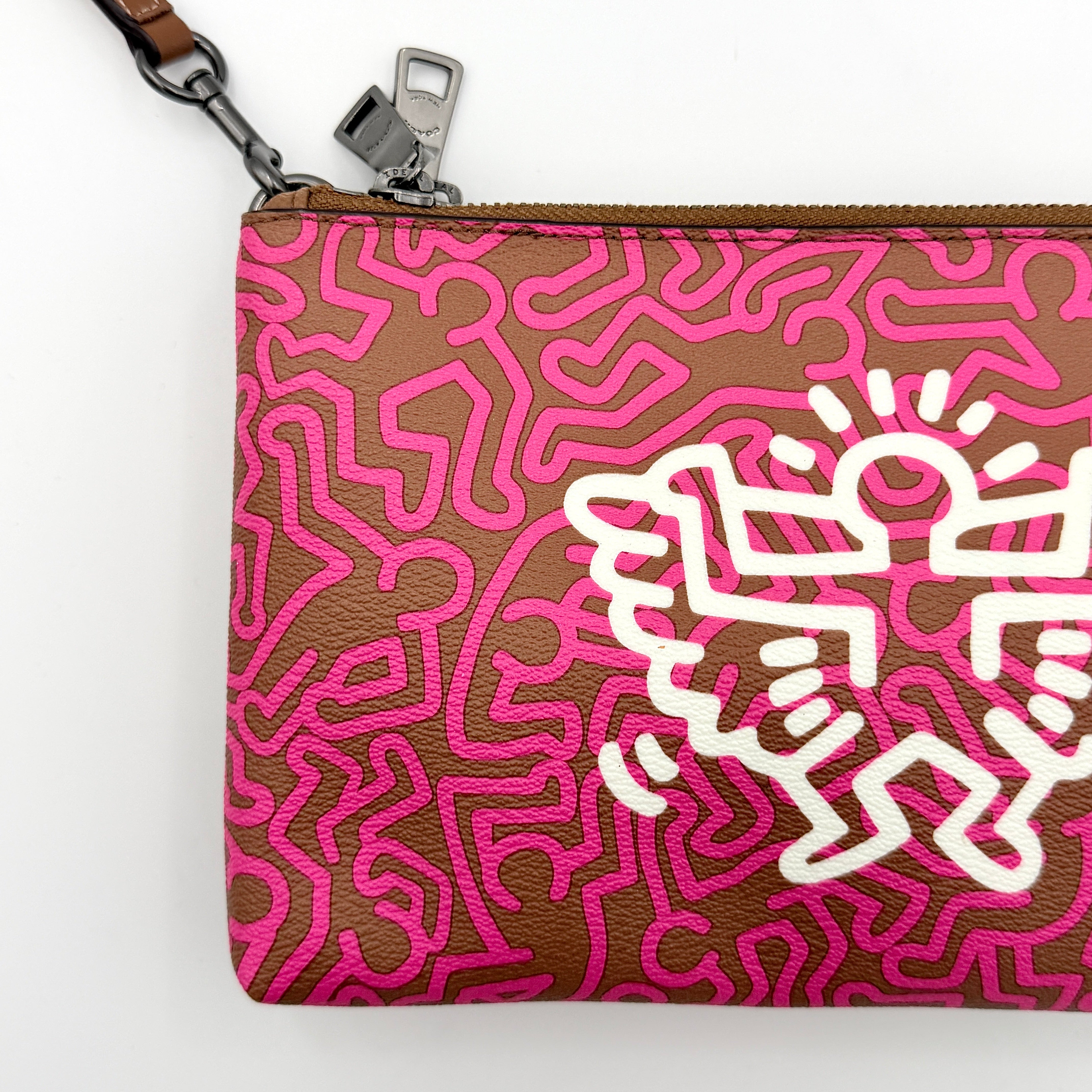 Coach x Keith Haring Lyla Crossbody bag in textured brown leather with bold pink graphic pattern and white artwork, featuring an adjustable strap.