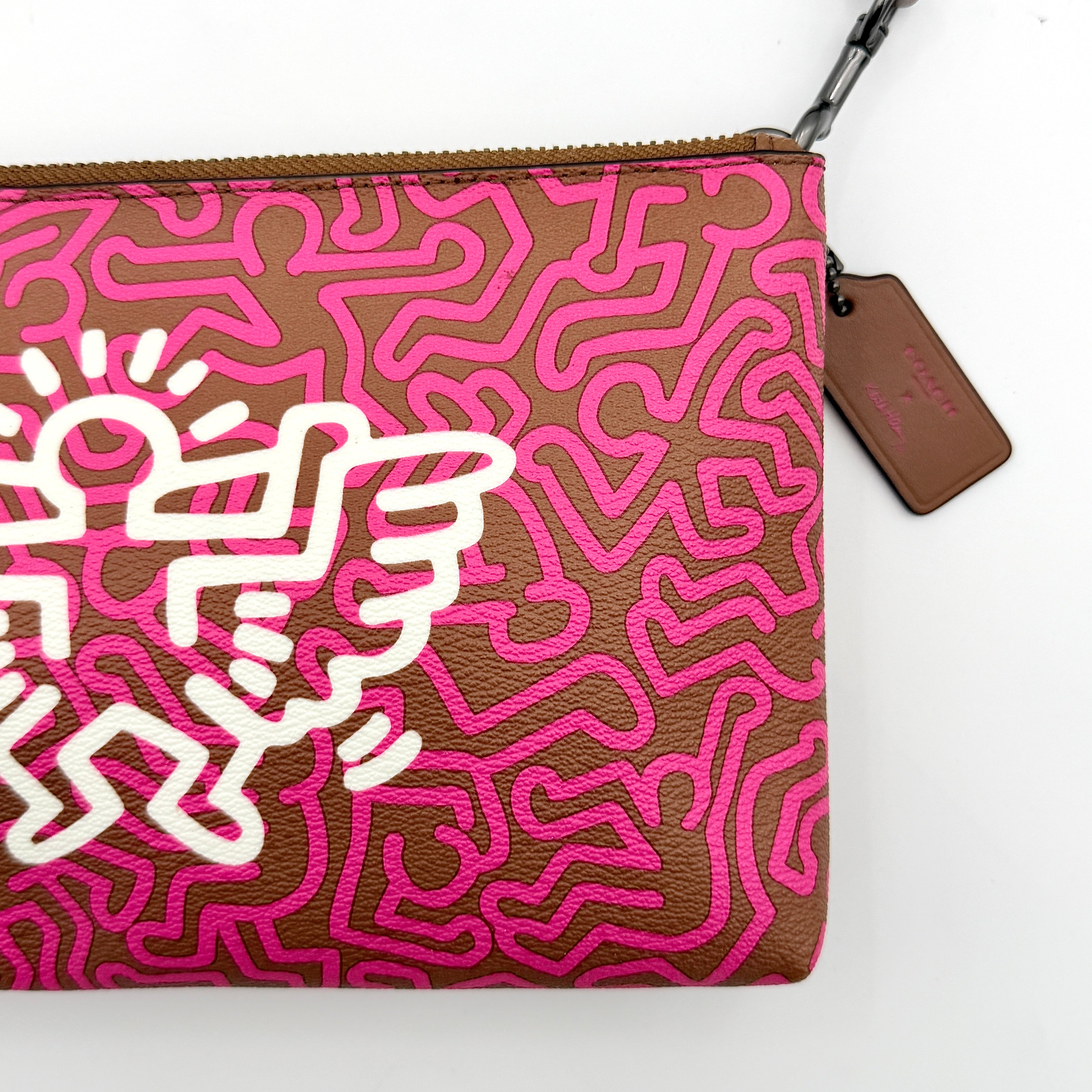 Coach x Keith Haring Lyla Crossbody bag in textured brown leather with bold pink graphic pattern and white artwork, featuring an adjustable strap.