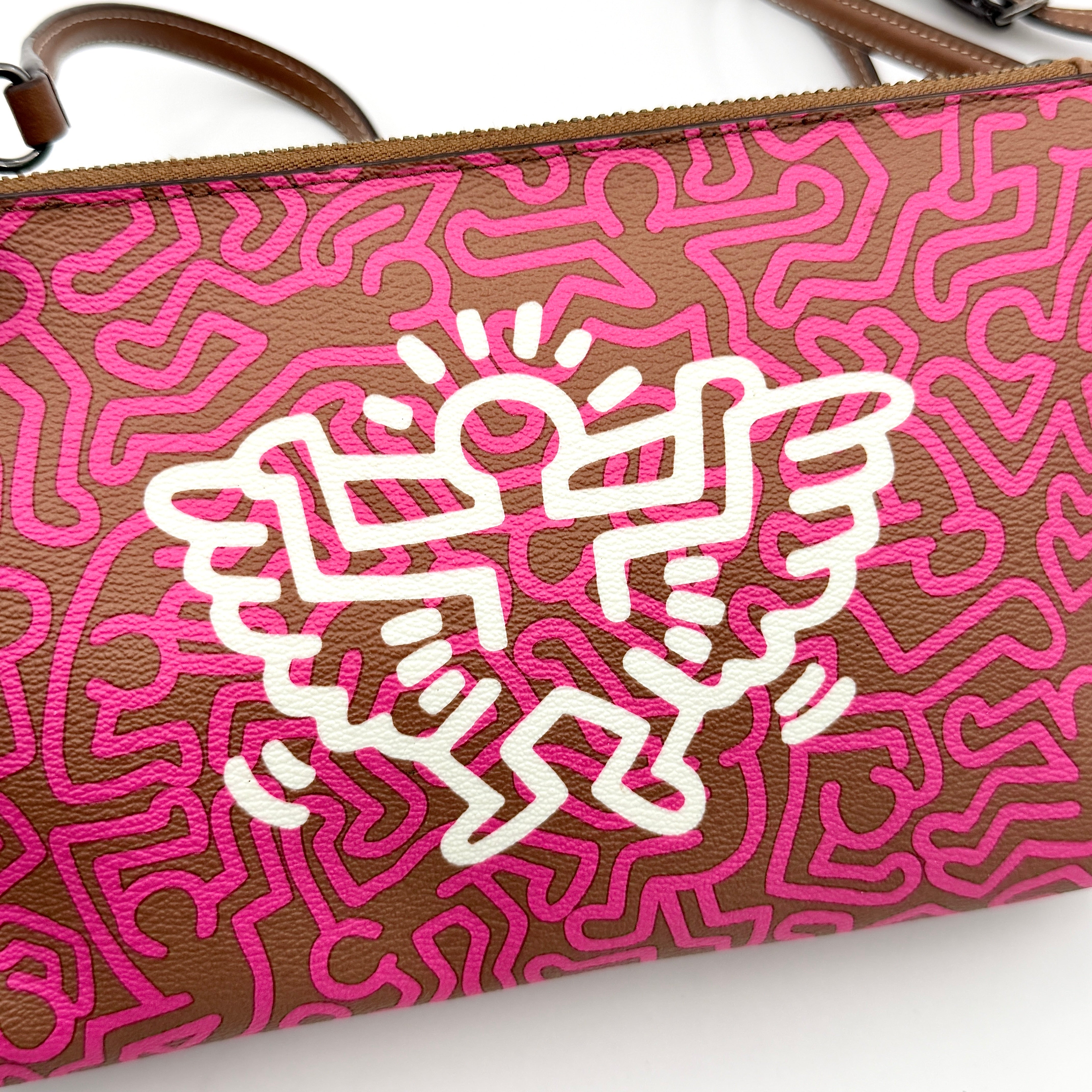 Coach x Keith Haring Lyla Crossbody bag in textured brown leather with bold pink graphic pattern and white artwork, featuring an adjustable strap.