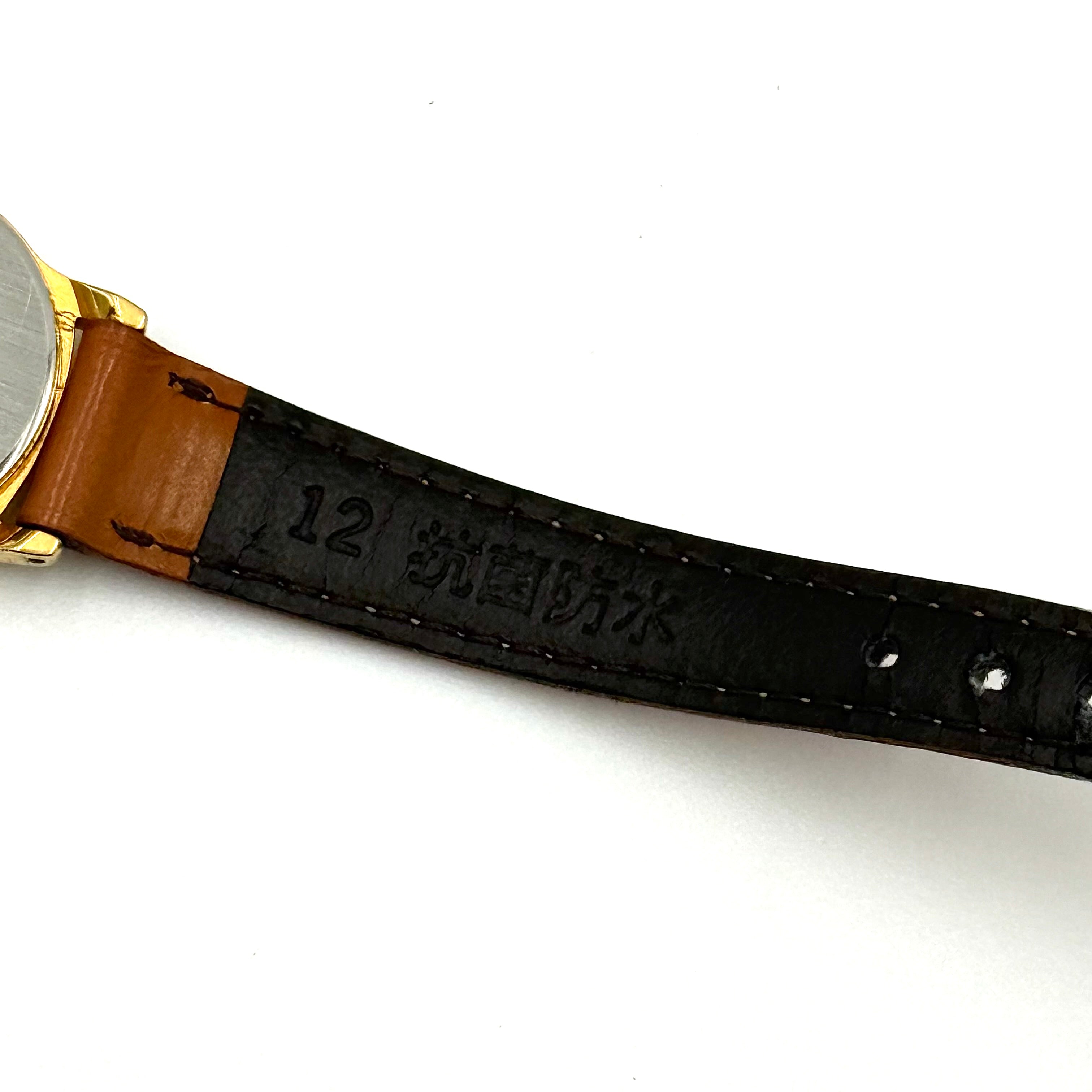 Seiko V701-A110 quartz watch with gold-tone case, cream dial, and brown leather strap on a display pillow.