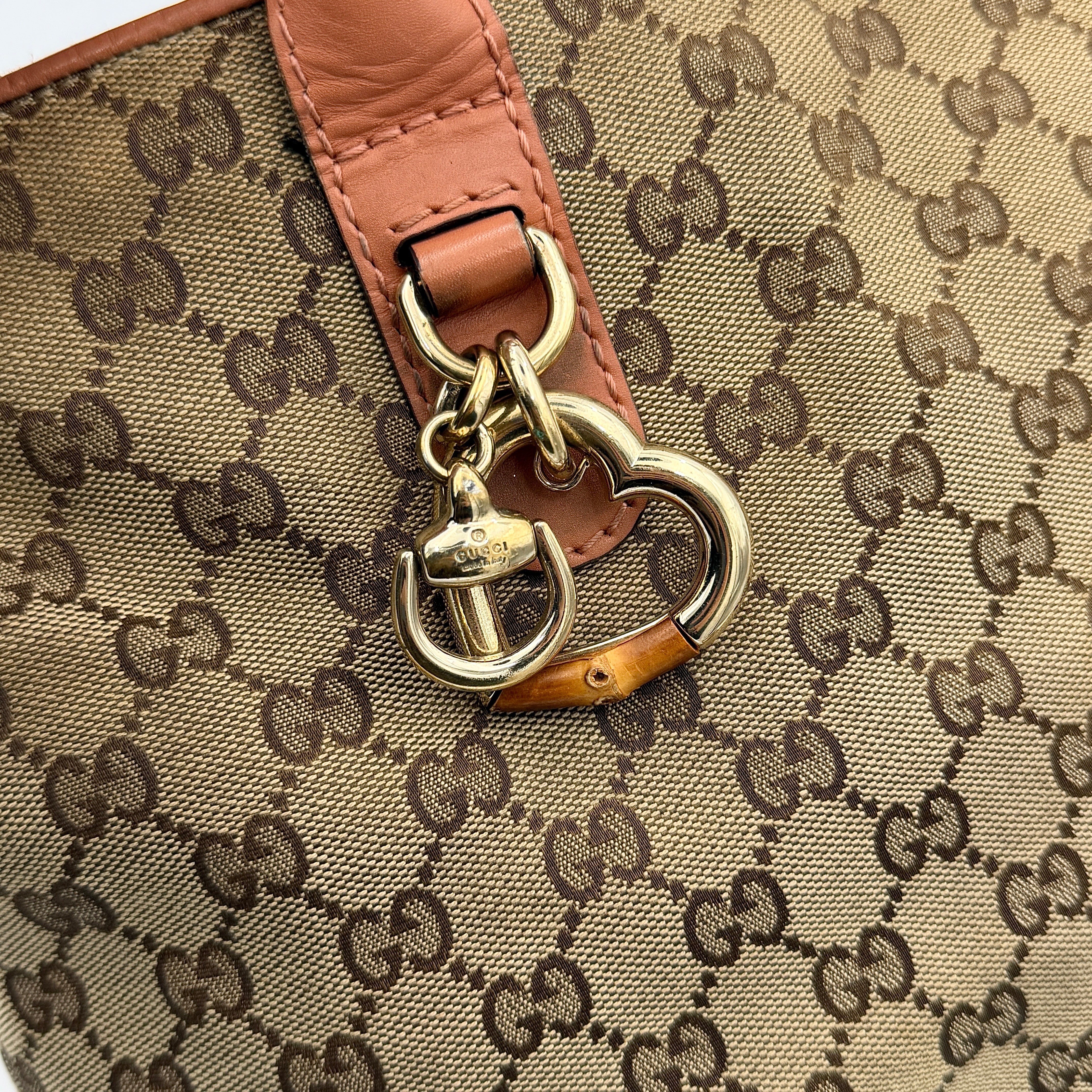 Gucci beige GG monogram shoulder bag with orange leather trim, heart bit charm, and detachable strap displayed on a white background.