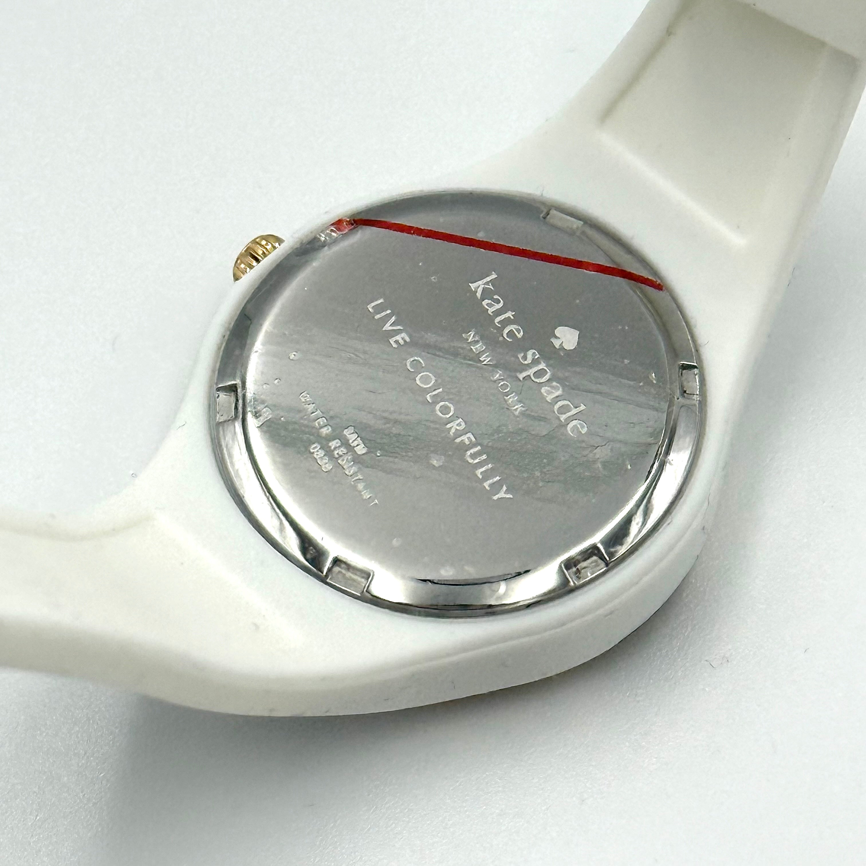 Kate Spade New York Rumsey 0838 silicone watch in white with black polka dots, gold-tone bezel, and white dial displayed on a cushion.