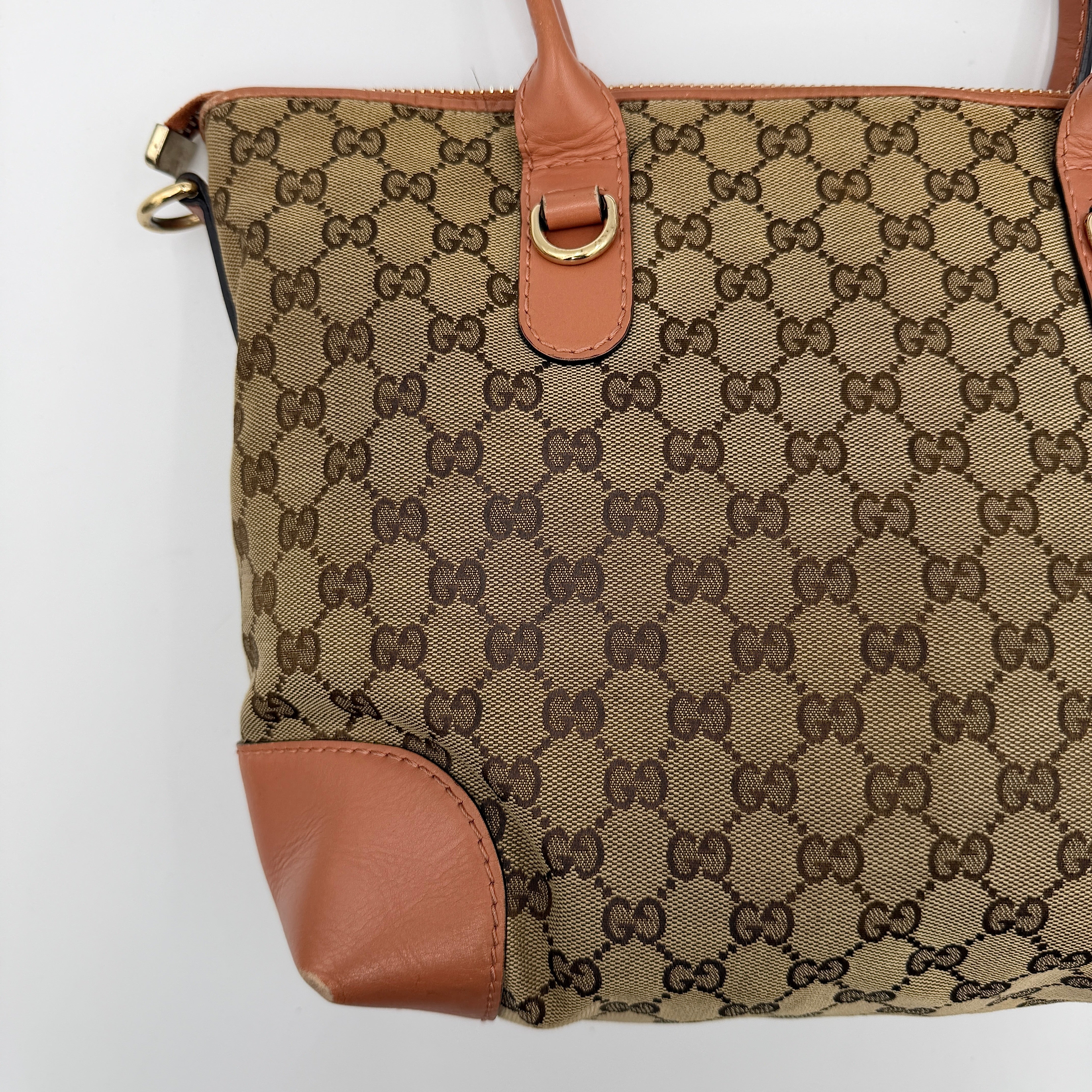 Gucci beige GG monogram shoulder bag with orange leather trim, heart bit charm, and detachable strap displayed on a white background.