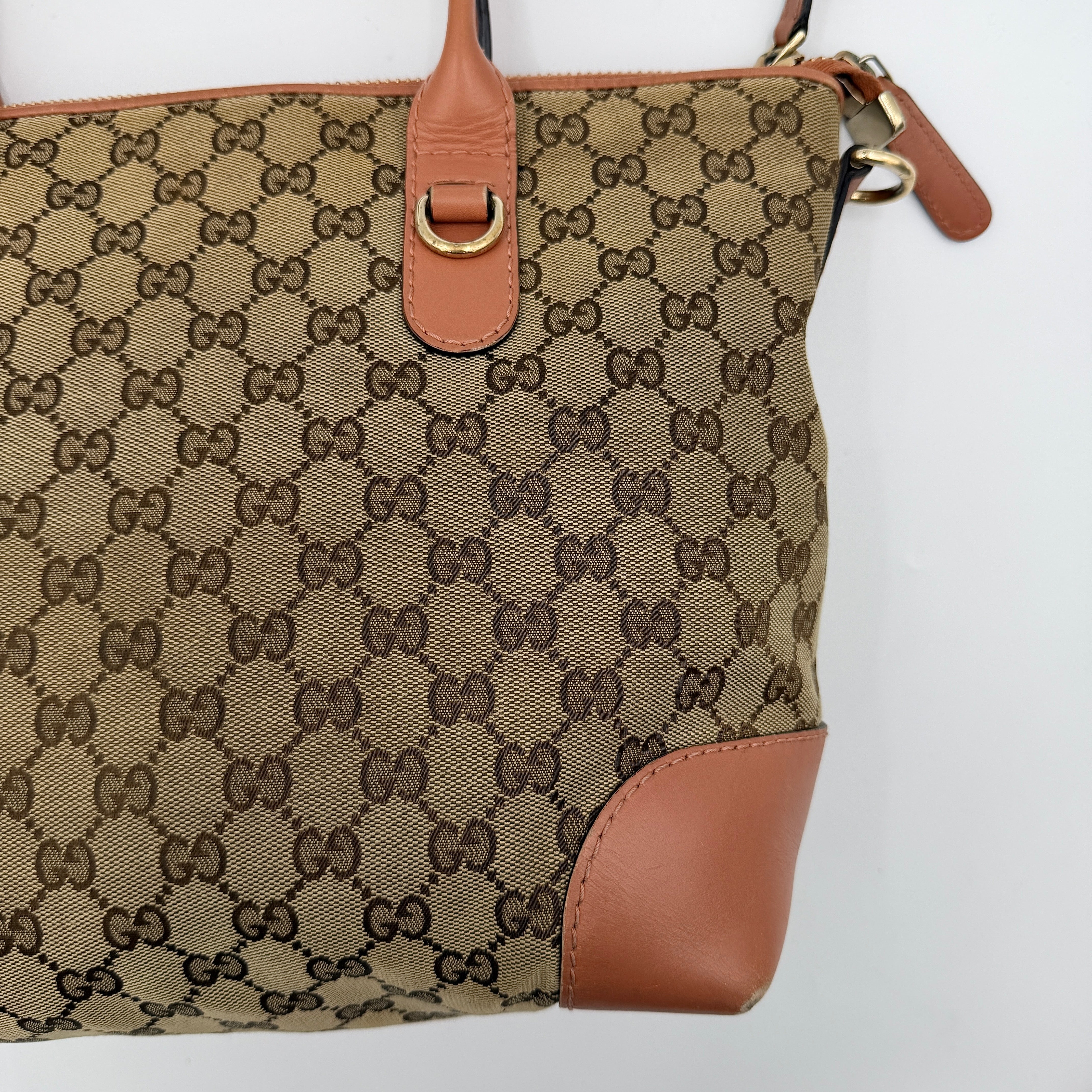 Gucci beige GG monogram shoulder bag with orange leather trim, heart bit charm, and detachable strap displayed on a white background.